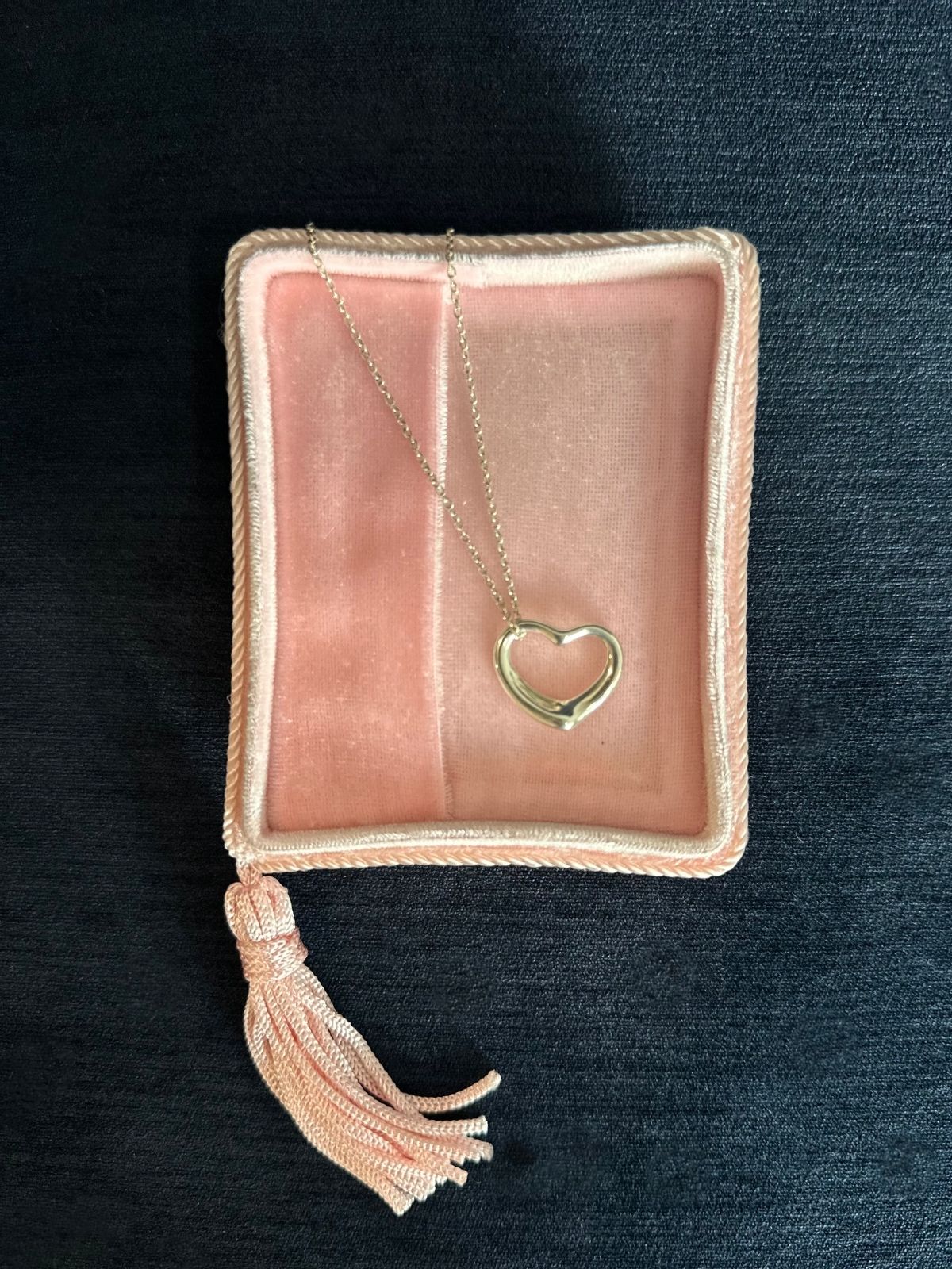Necklace with a heart pendant on a pink jewelry pouch against a dark background