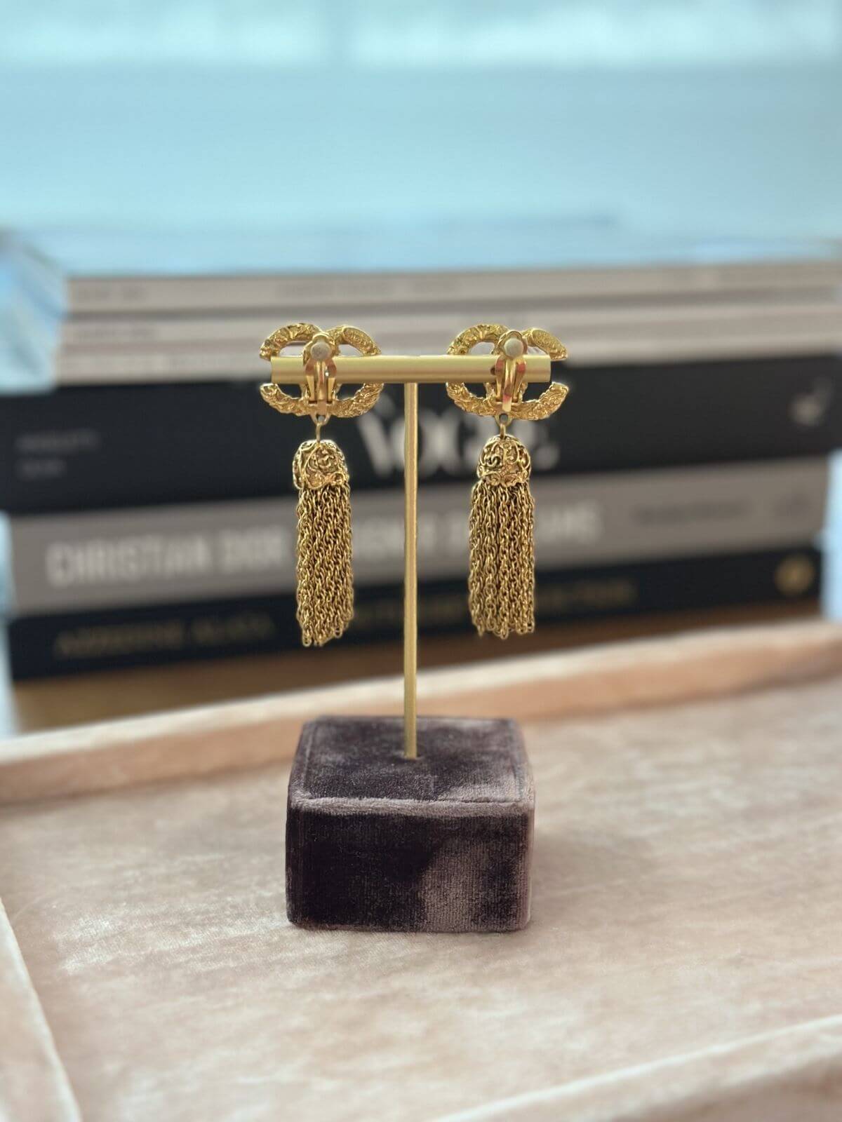 Gold earrings on a stand with a blurred bookshelf in the background