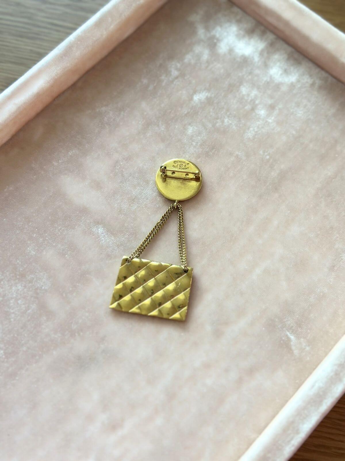 Chanel Gold brooch with a bag design on a pink surface