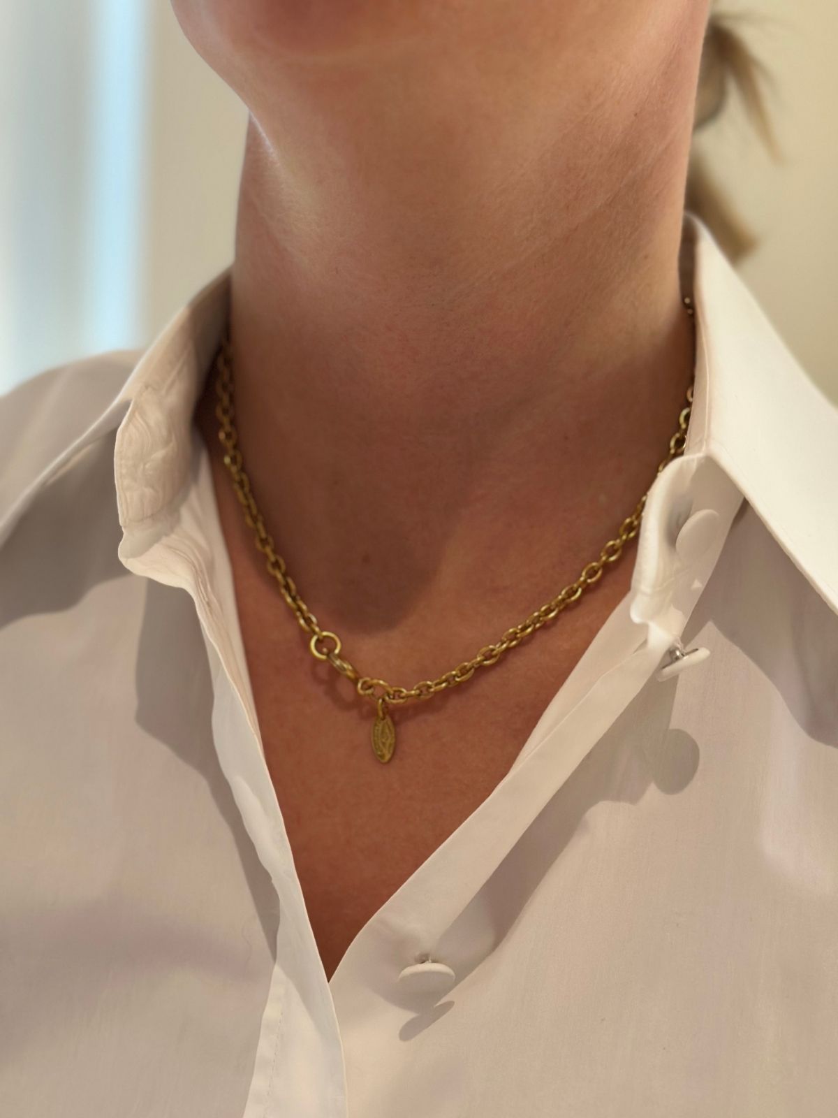 Gold chanel chain on model in white shirt close up of neckline.