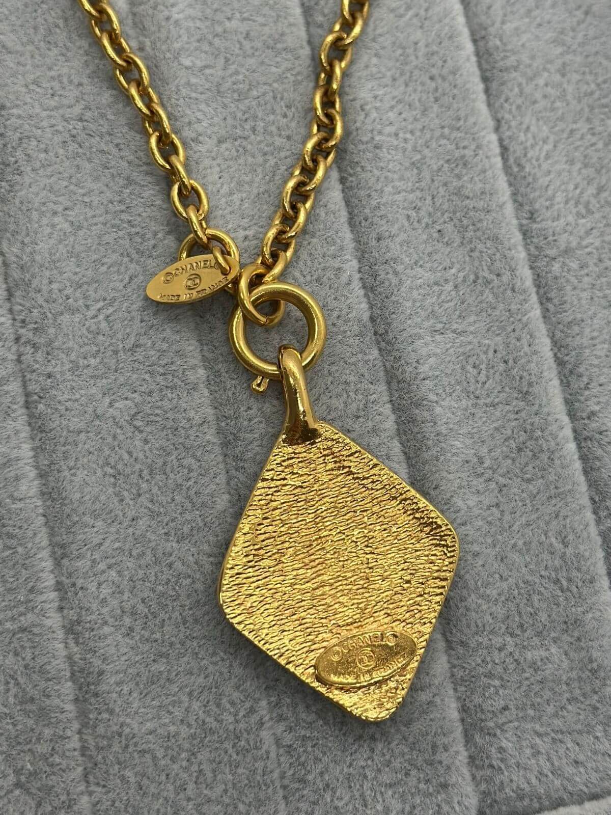 Back of diamond shaped gold Chanel necklace on grey soft fixture.