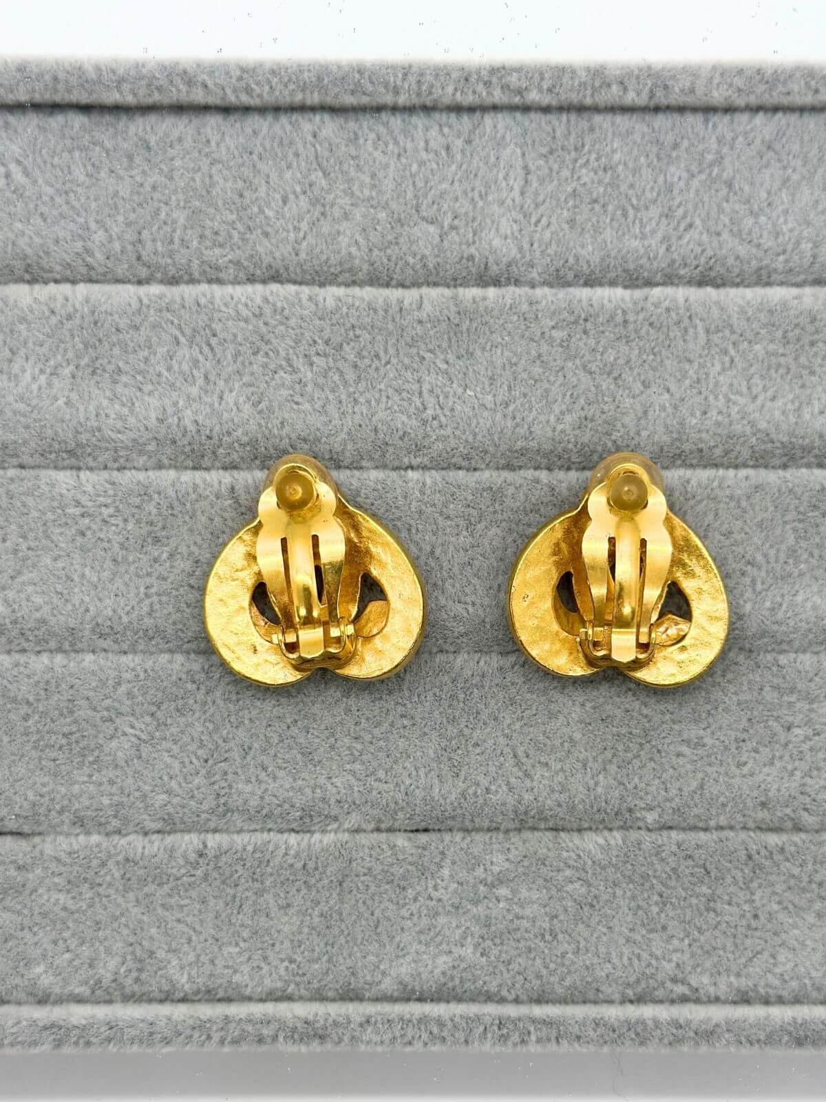 Chanel gold clip on heart earring on grey fixture. Back side.