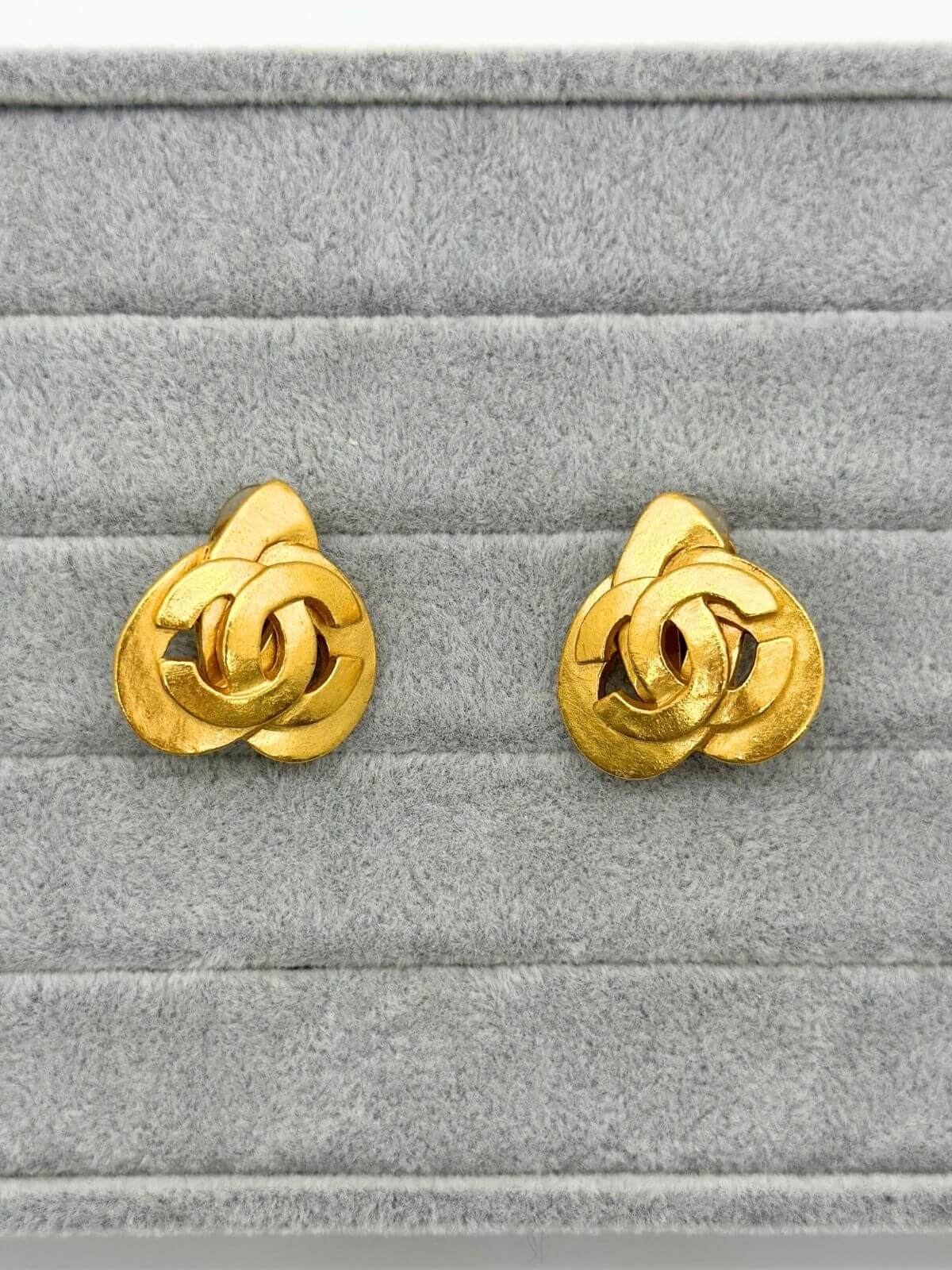 Chanel gold clip on heart earring on grey fixture.