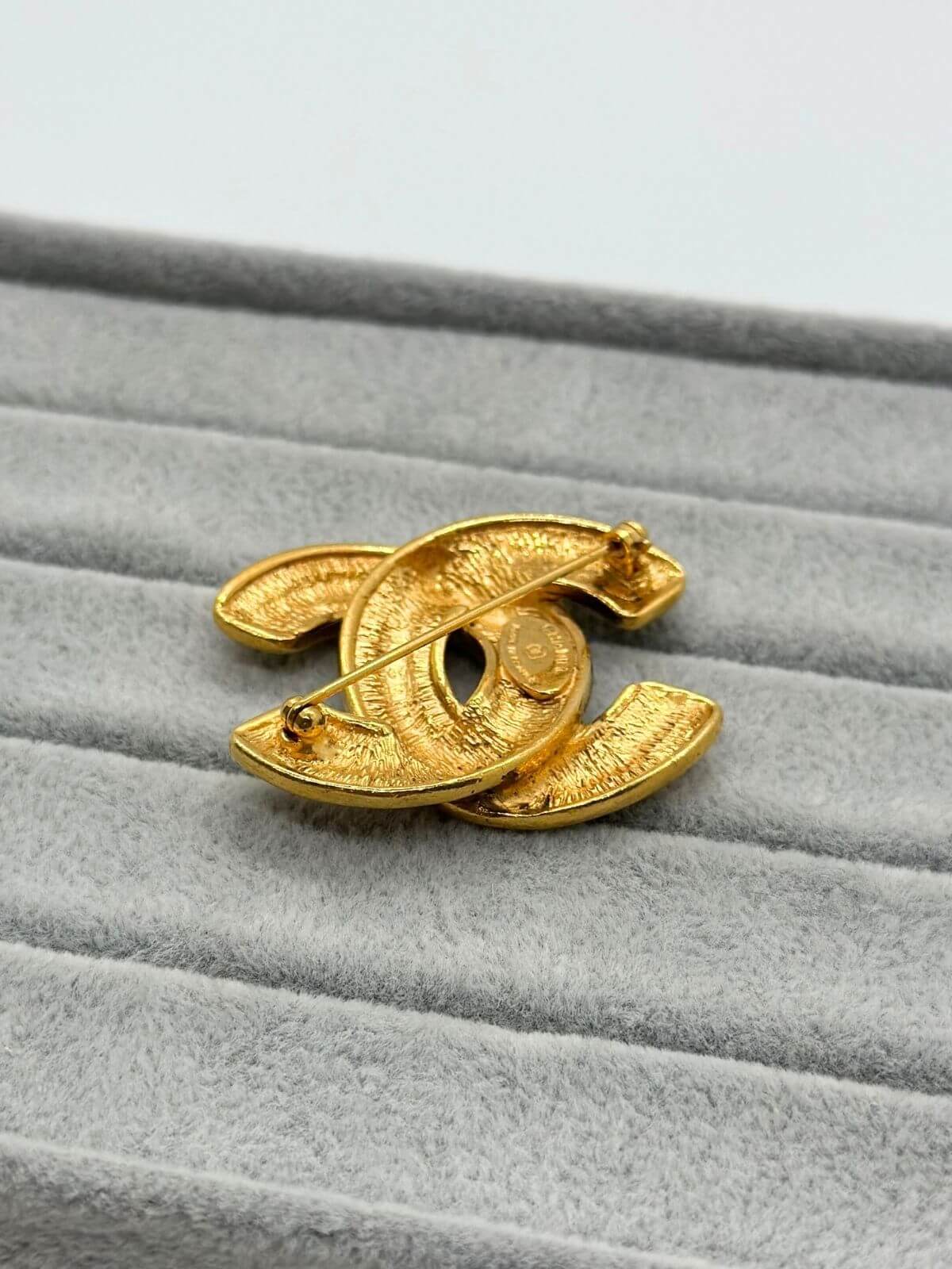 Gold quilted Chanel brooch on grey background. Back side .