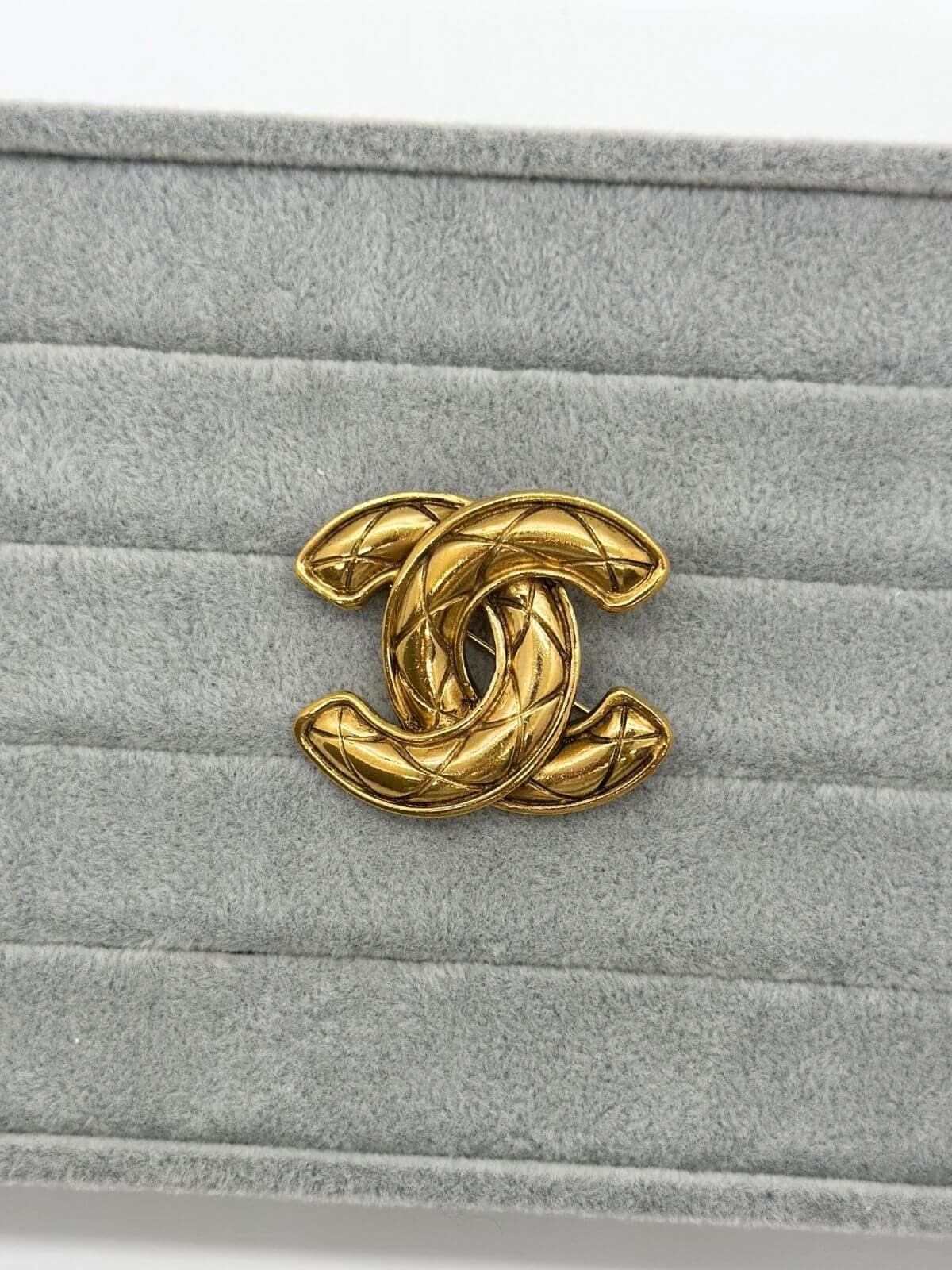 Gold quilted Chanel brooch on grey background.