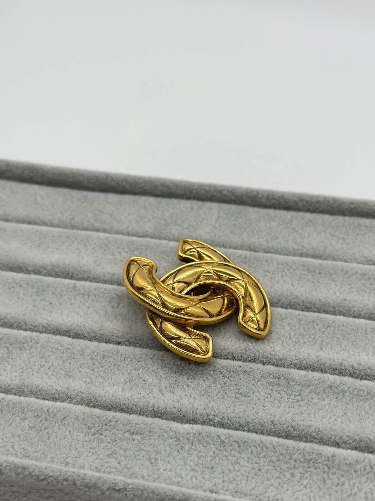 Gold quilted Chanel brooch on grey background.