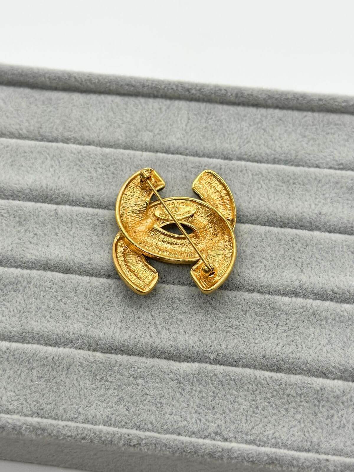 Gold quilted Chanel brooch on grey background. Back Side