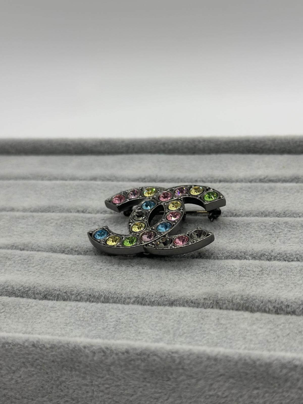 Pre-loved Chanel Multi color brooch on grey background side view
