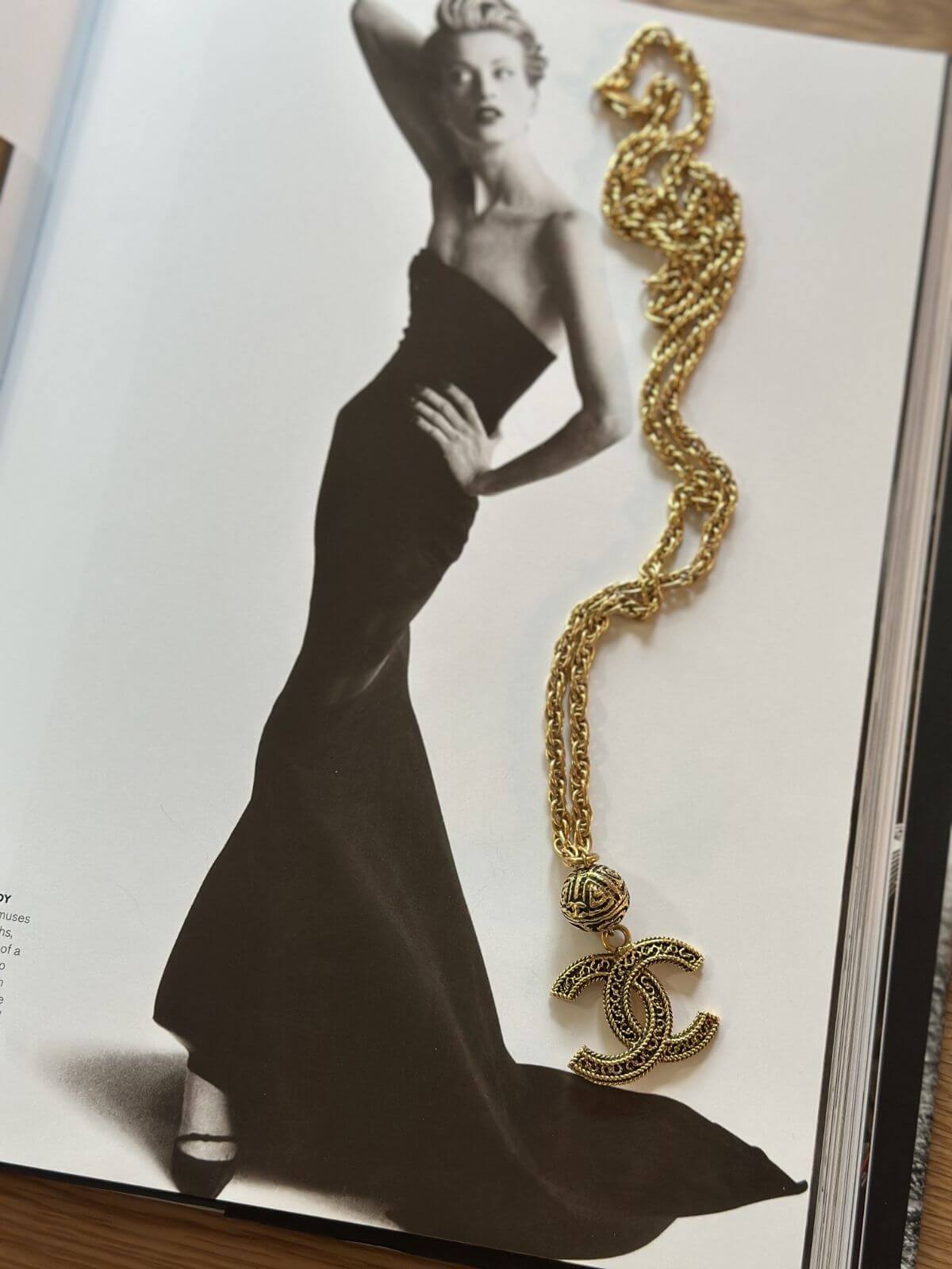 Gold Chanel necklace on a magazine with a black and white photo of a woman in a long dress.