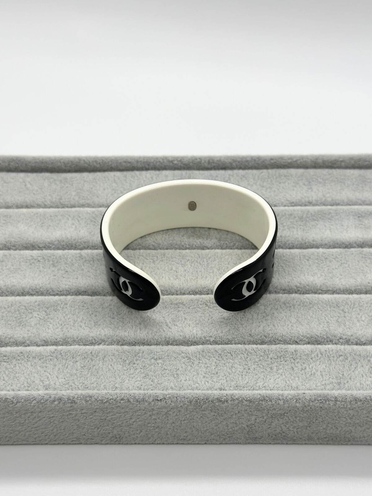 Chanel black and white resin CC cuff on grey background.