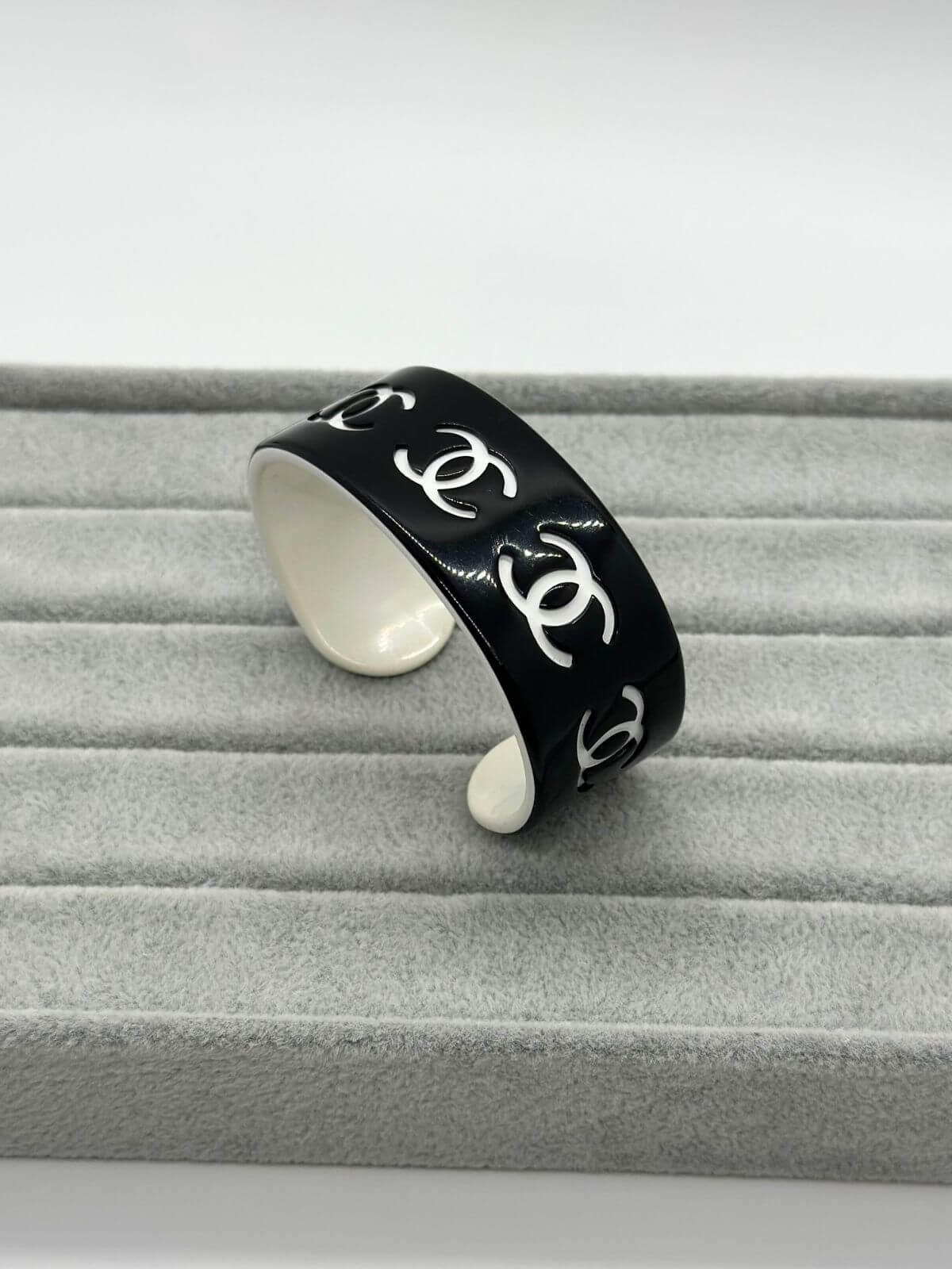 Chanel black and white resin CC cuff on grey background.