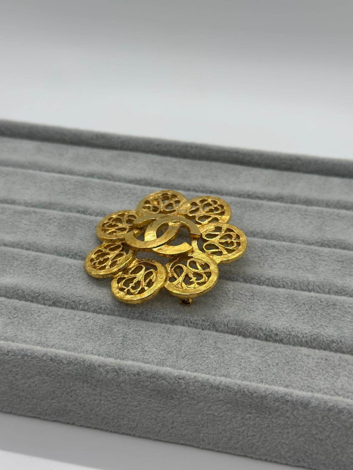 Vintage Chanel Gold sphere brooch on a grey fabric background