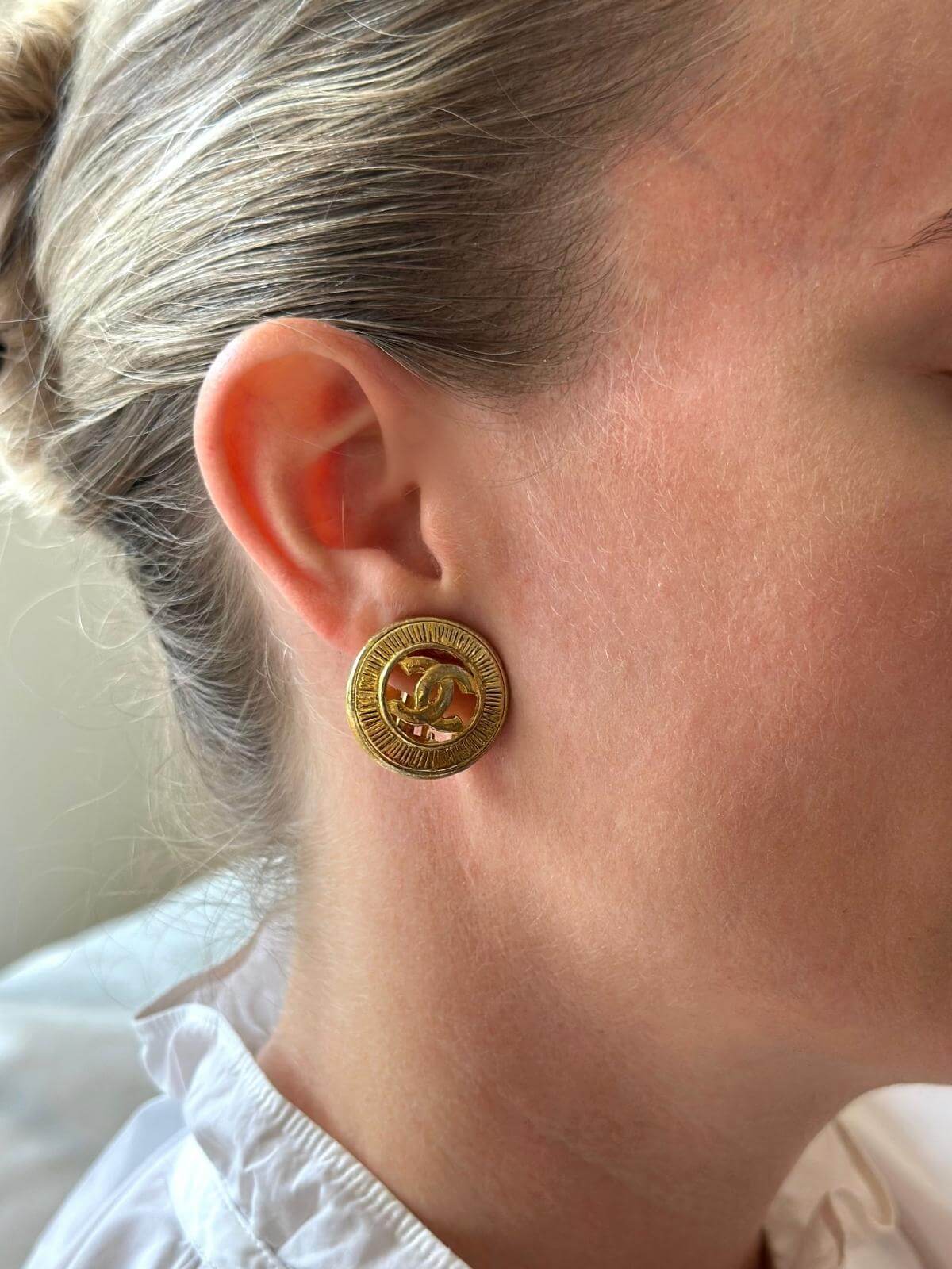 Model in white shirt close up wearing gold Chanel earrings.