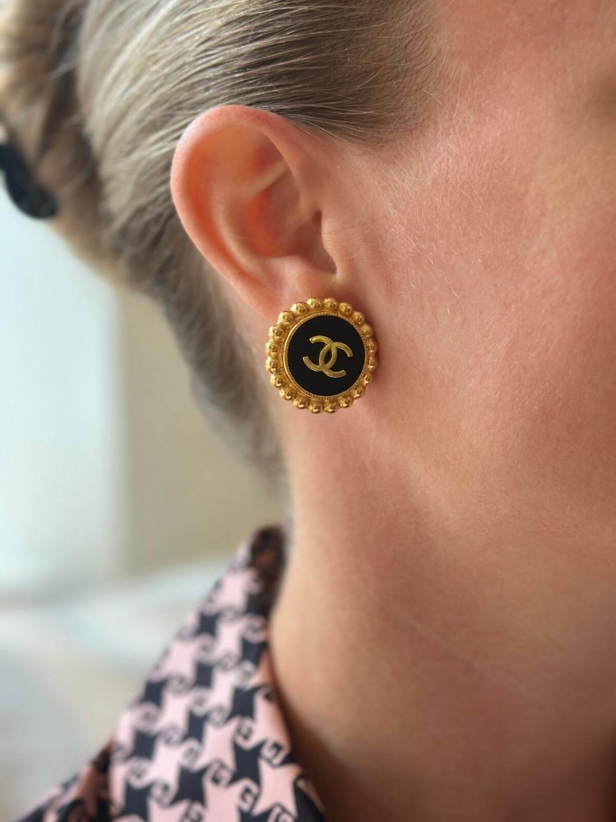 Model wearing Chanel button earrings with black and gold design.