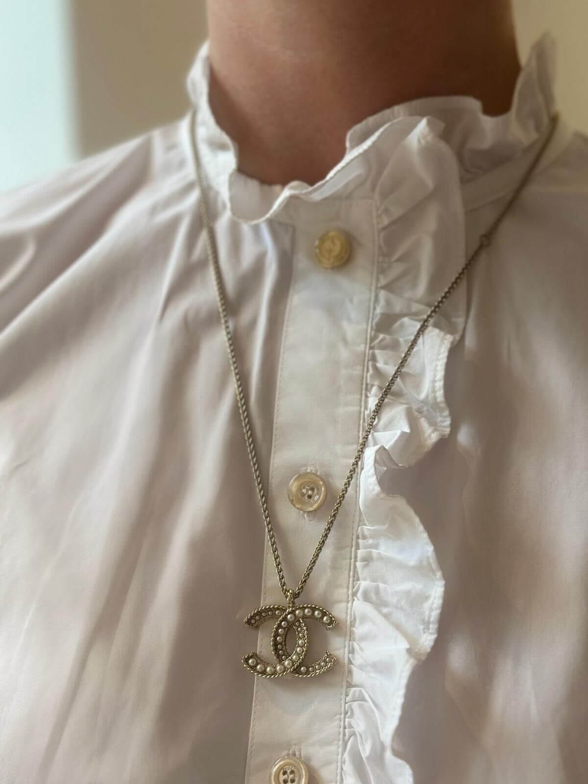 MOdel in white blouse wearing Chanel pearl and gold necklace.