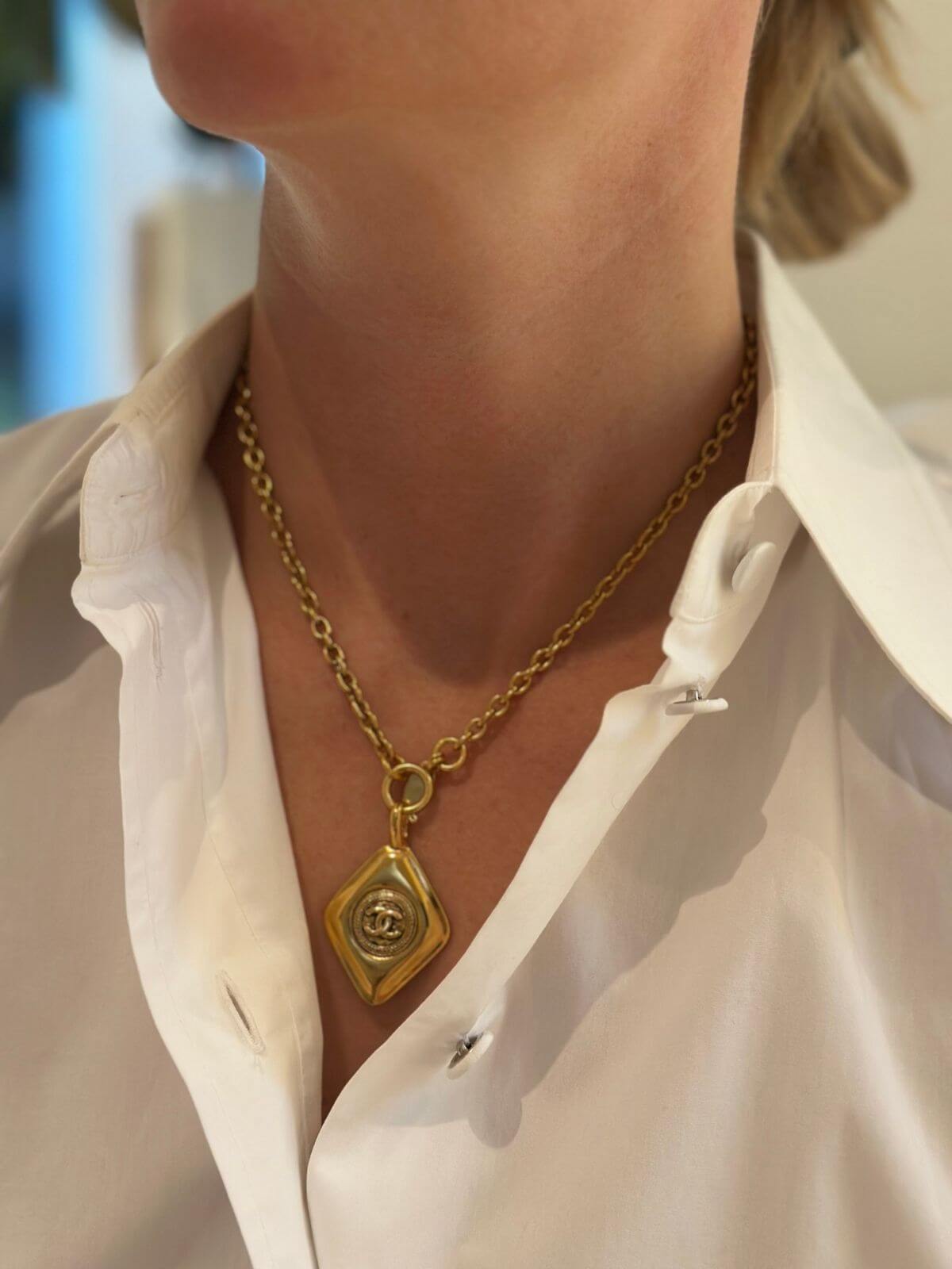 Gold diamond shaped Chanel necklace on model close up in white shirt.