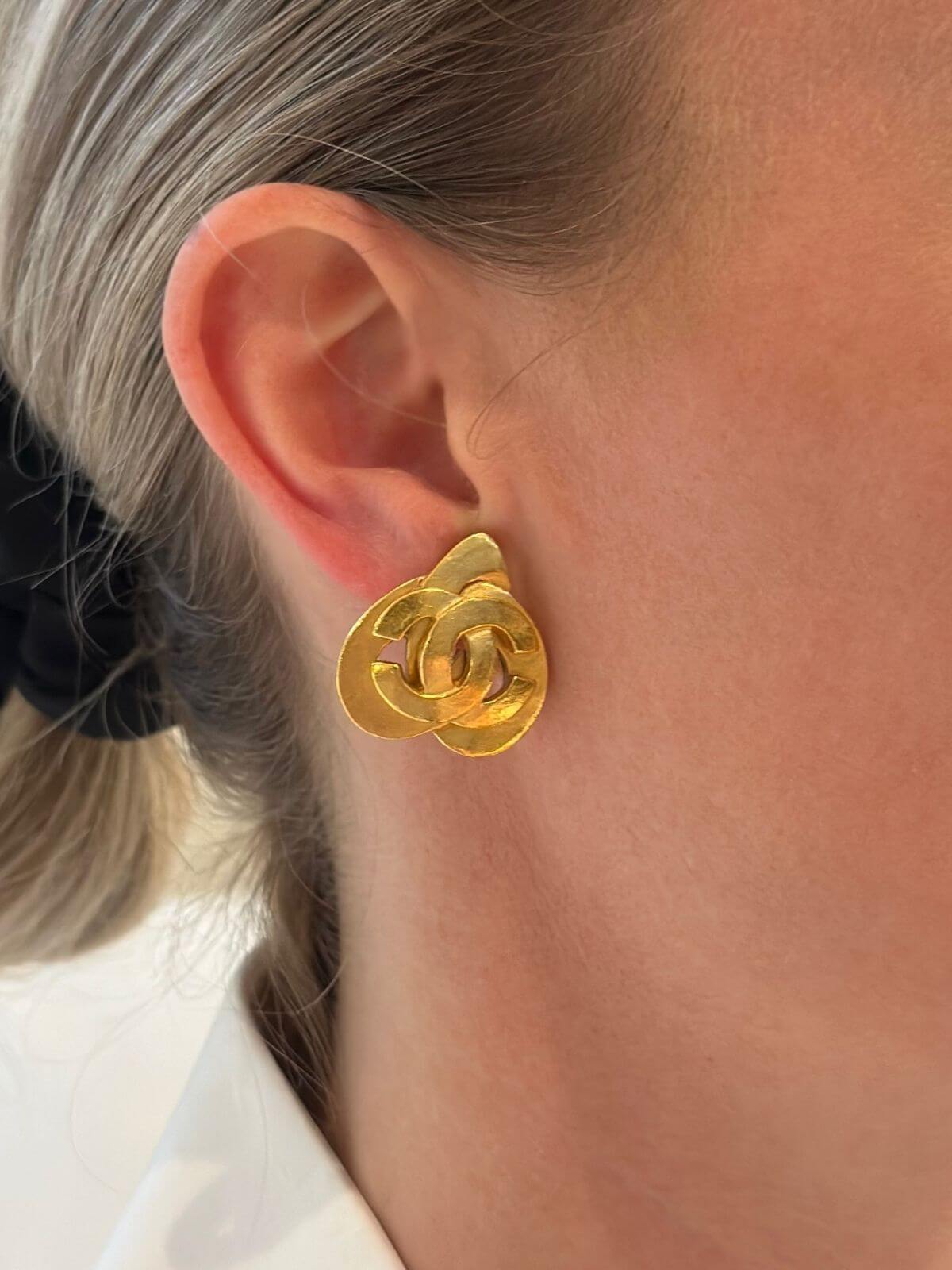 Chanel gold heart earring on model close up of ear.