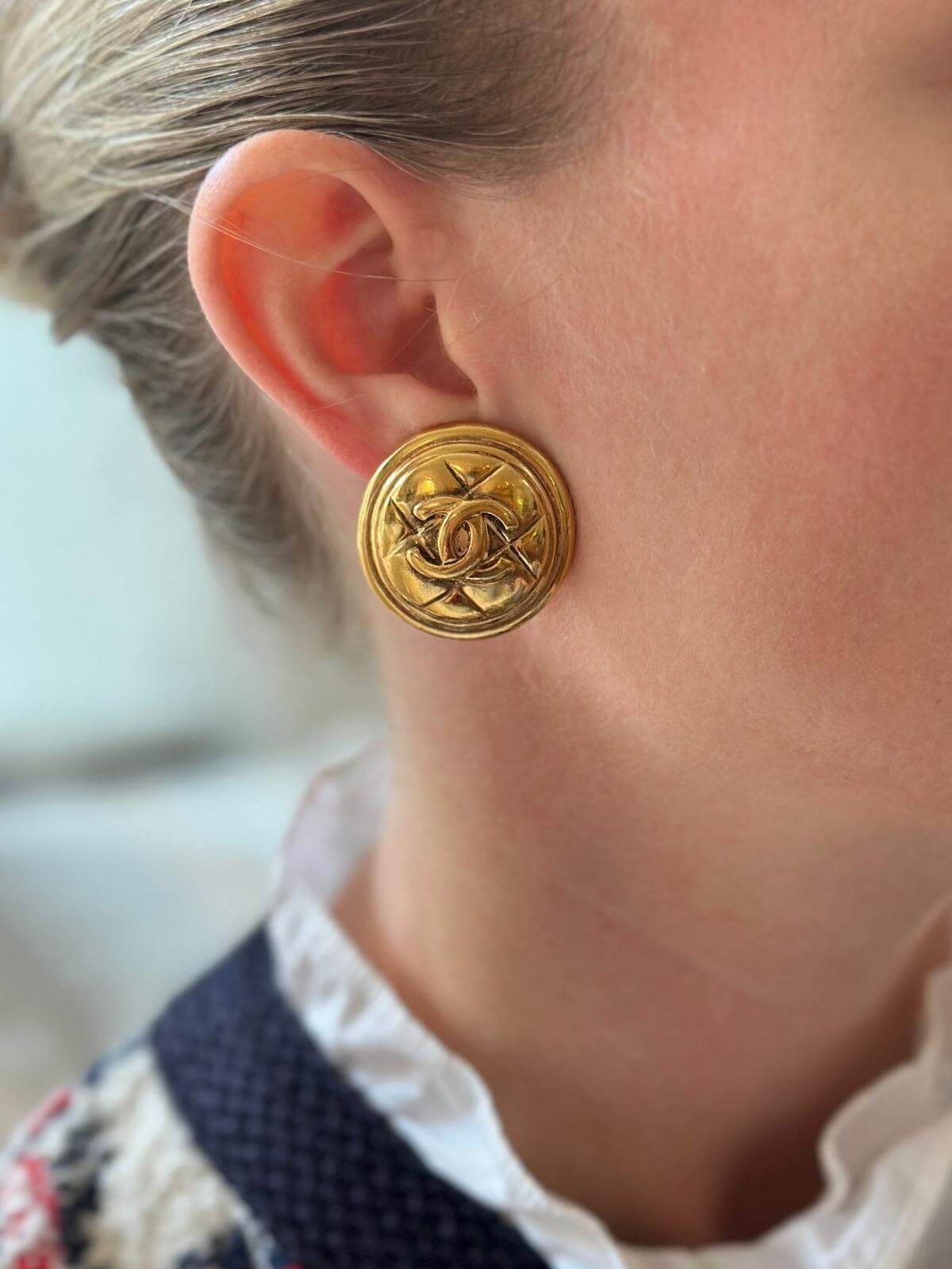 Model wearing gold Chanel quilted clip on earrings, close up.