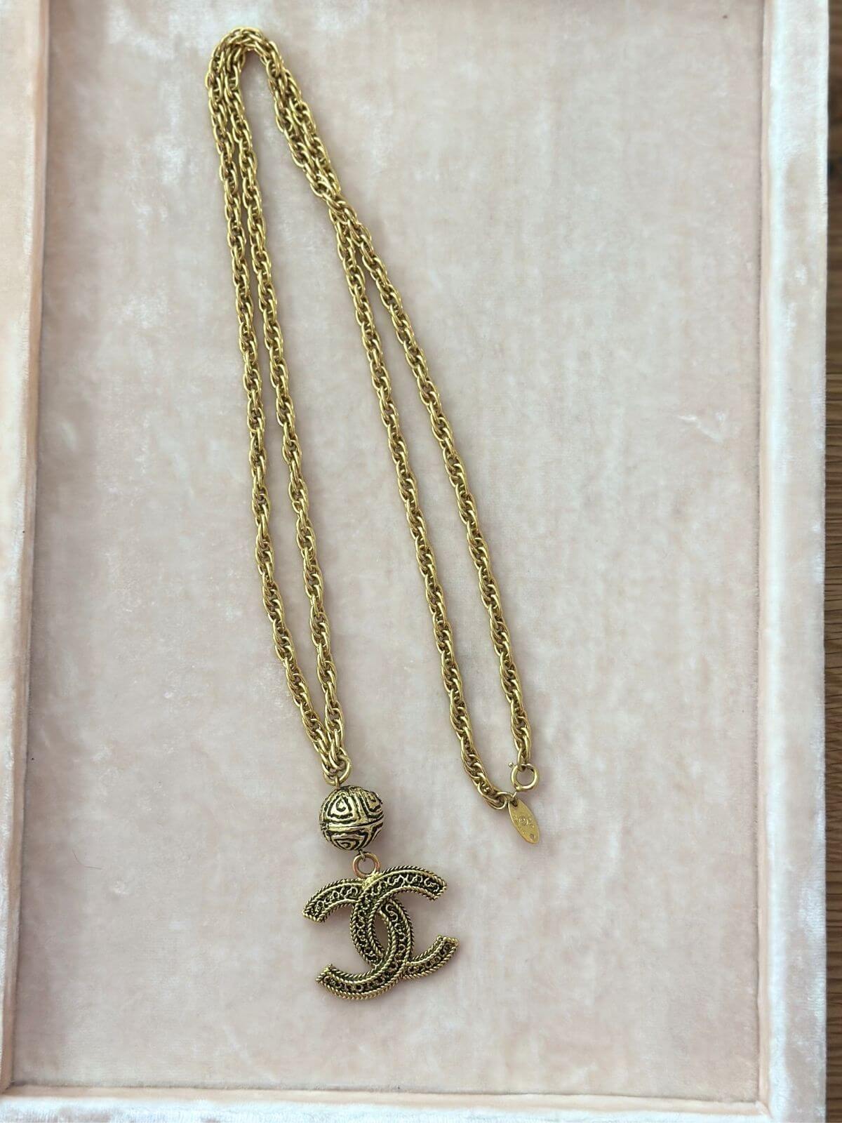 Gold necklace with a CC pendant on a beige background