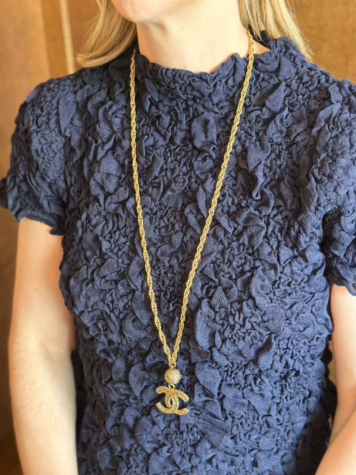Person wearing a navy lace top with a gold necklace featuring a Chanel logo.