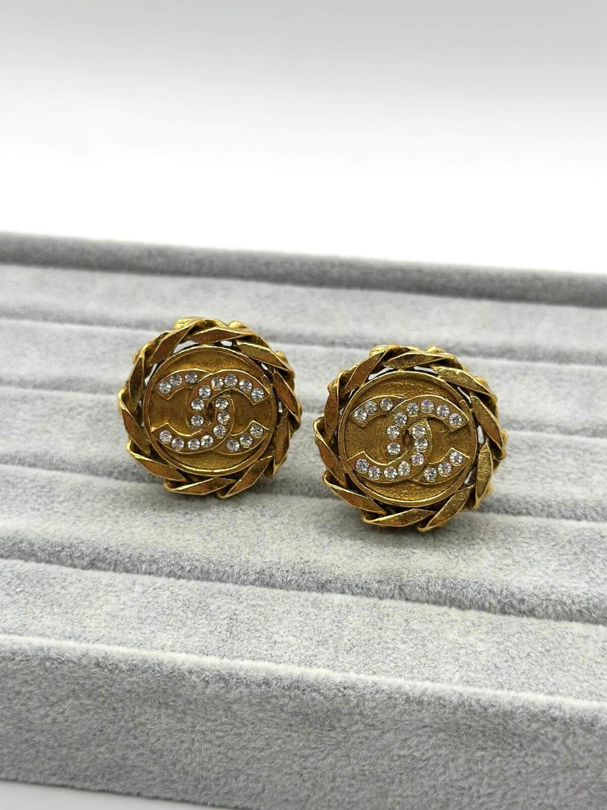 Chanel gold round clip on earring with crystal on grey and white background.