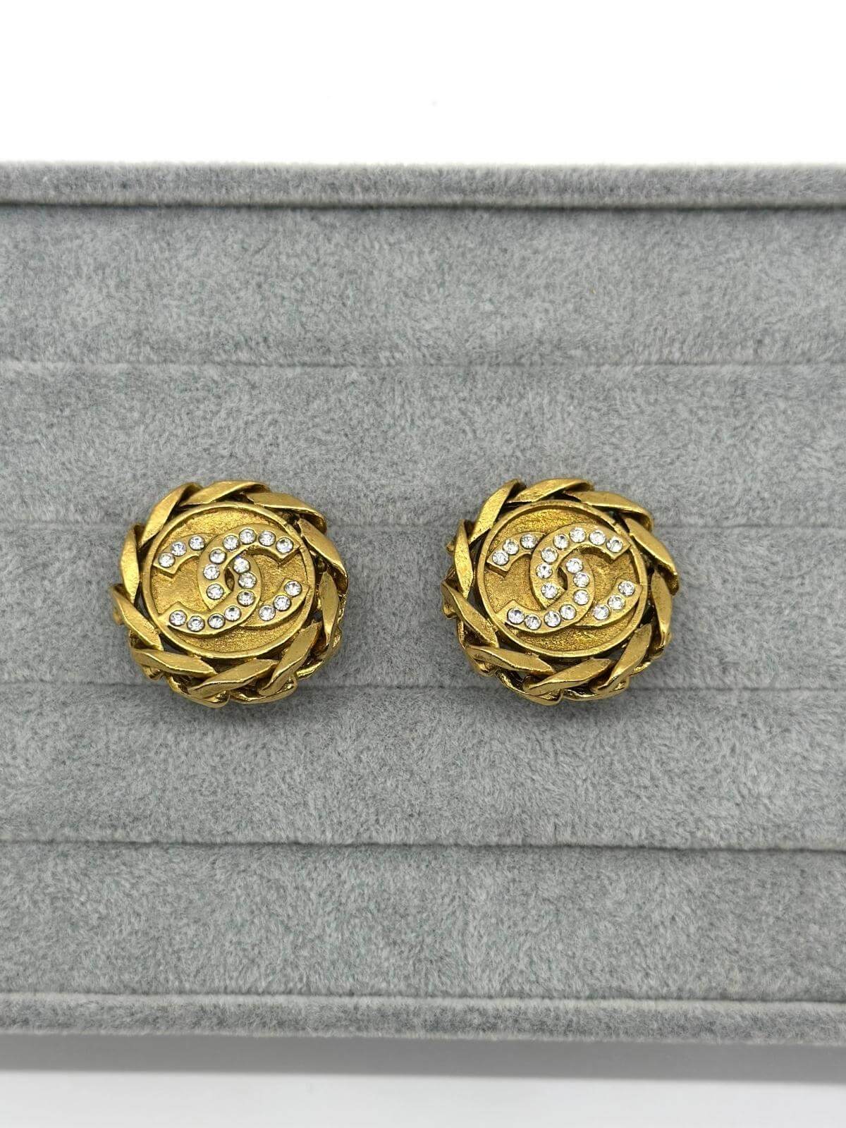 Chanel gold round clip on earring with crystal on grey and white background.