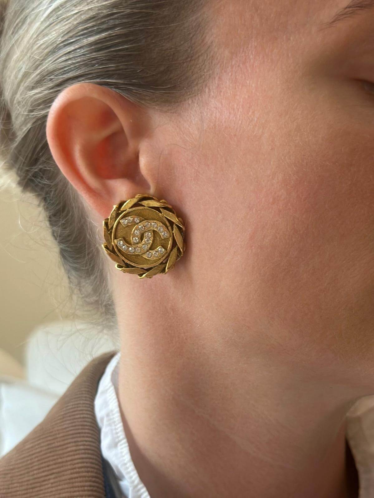 Model close up wearing gold and crystal Chanel earrings.