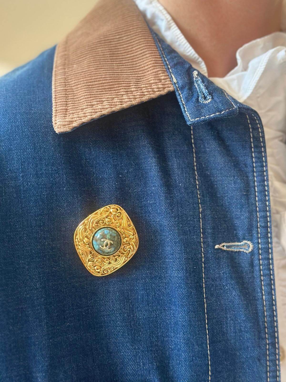 Model in jean jacket wearing turquoise Chanel gold brooch.