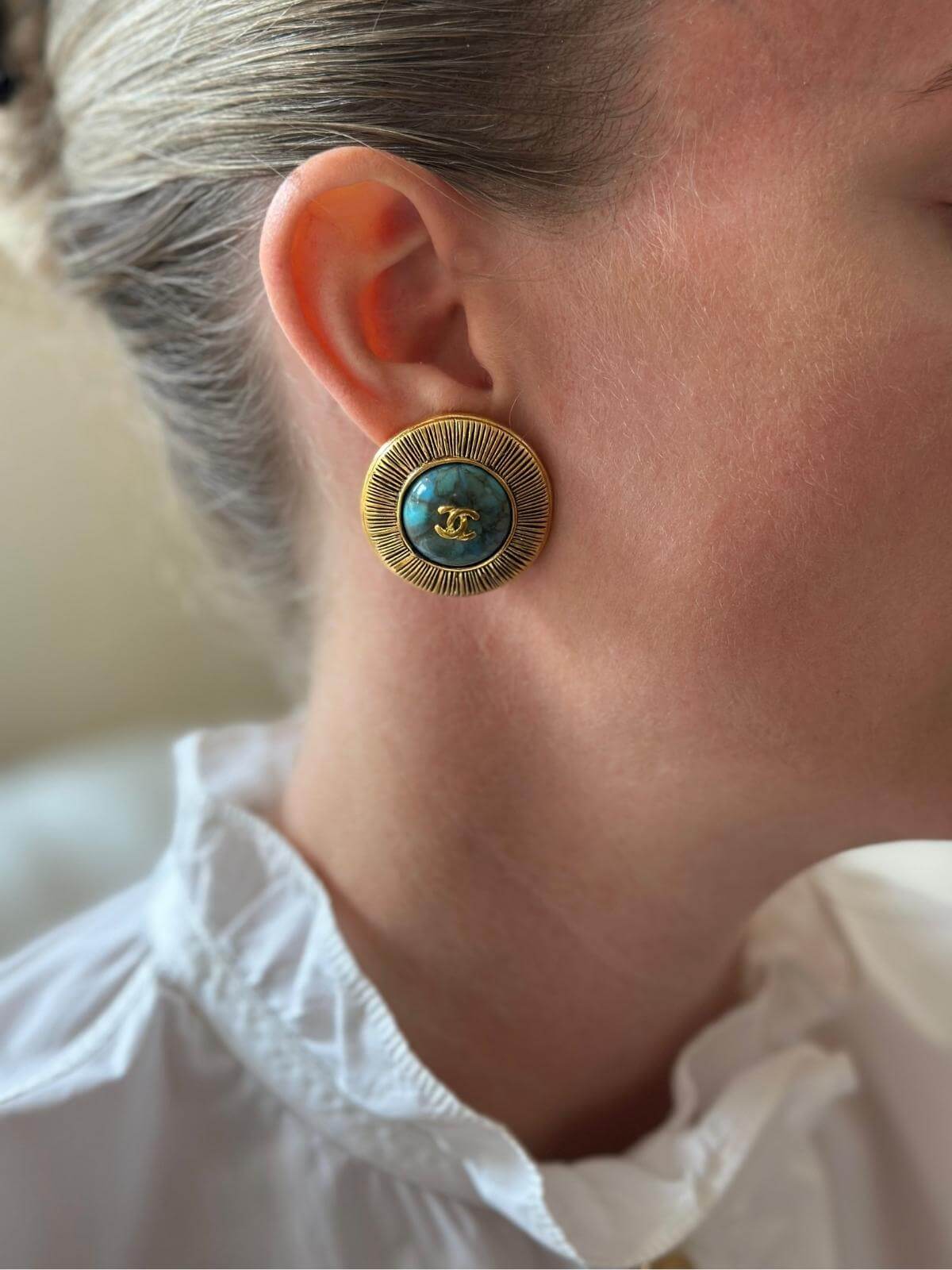 Close up of model wearing turquoise and gold Chanel earrings.
