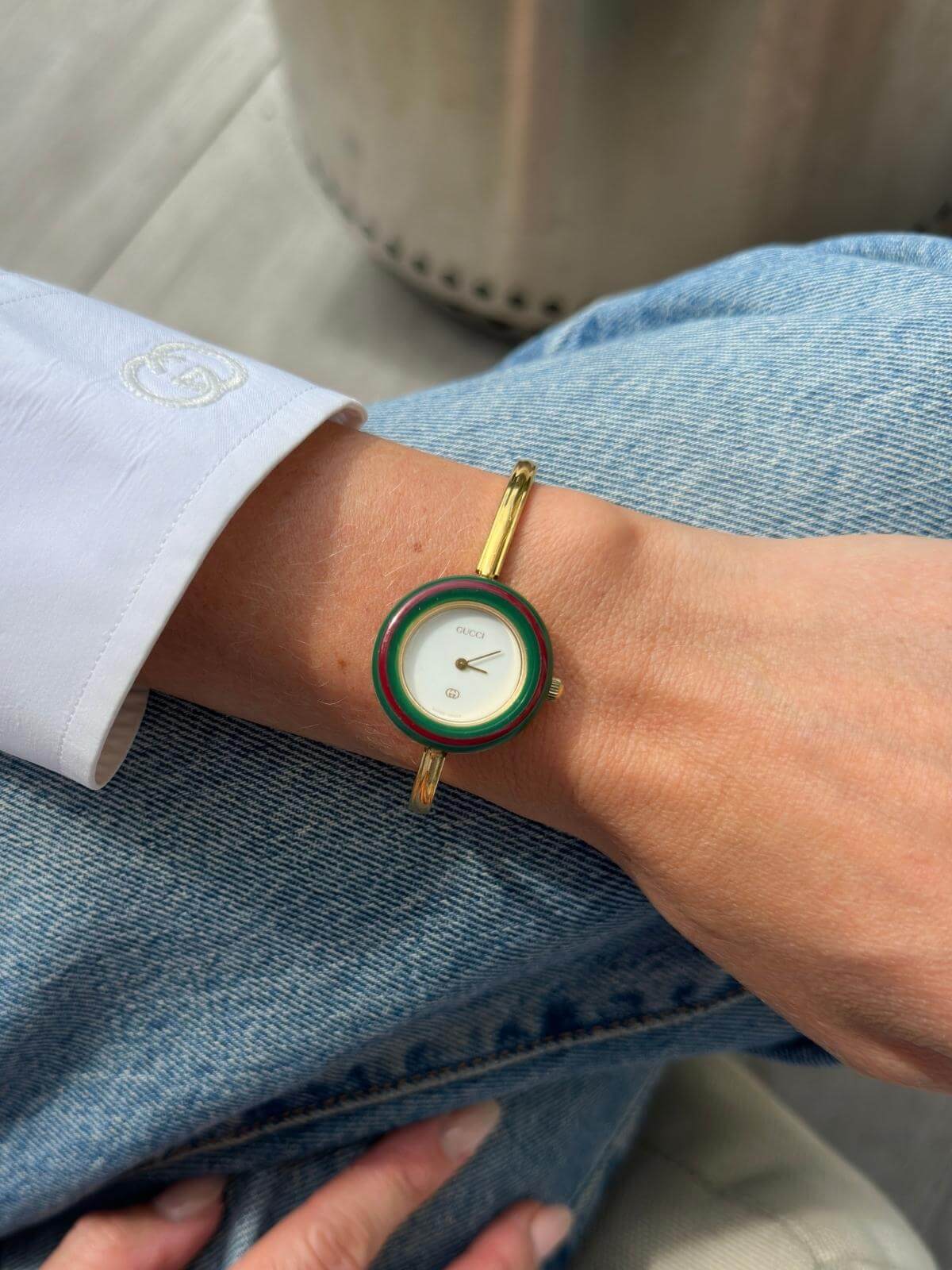 Close-up of a wrist wearing a Gucci gold and green watch with a blurred background