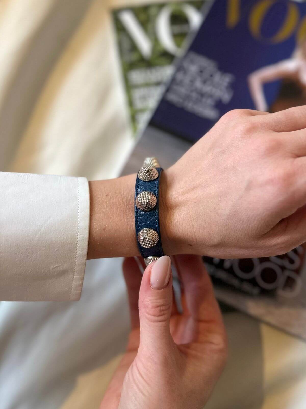Hand wearing Balenciaga studded bracelet on a magazine background