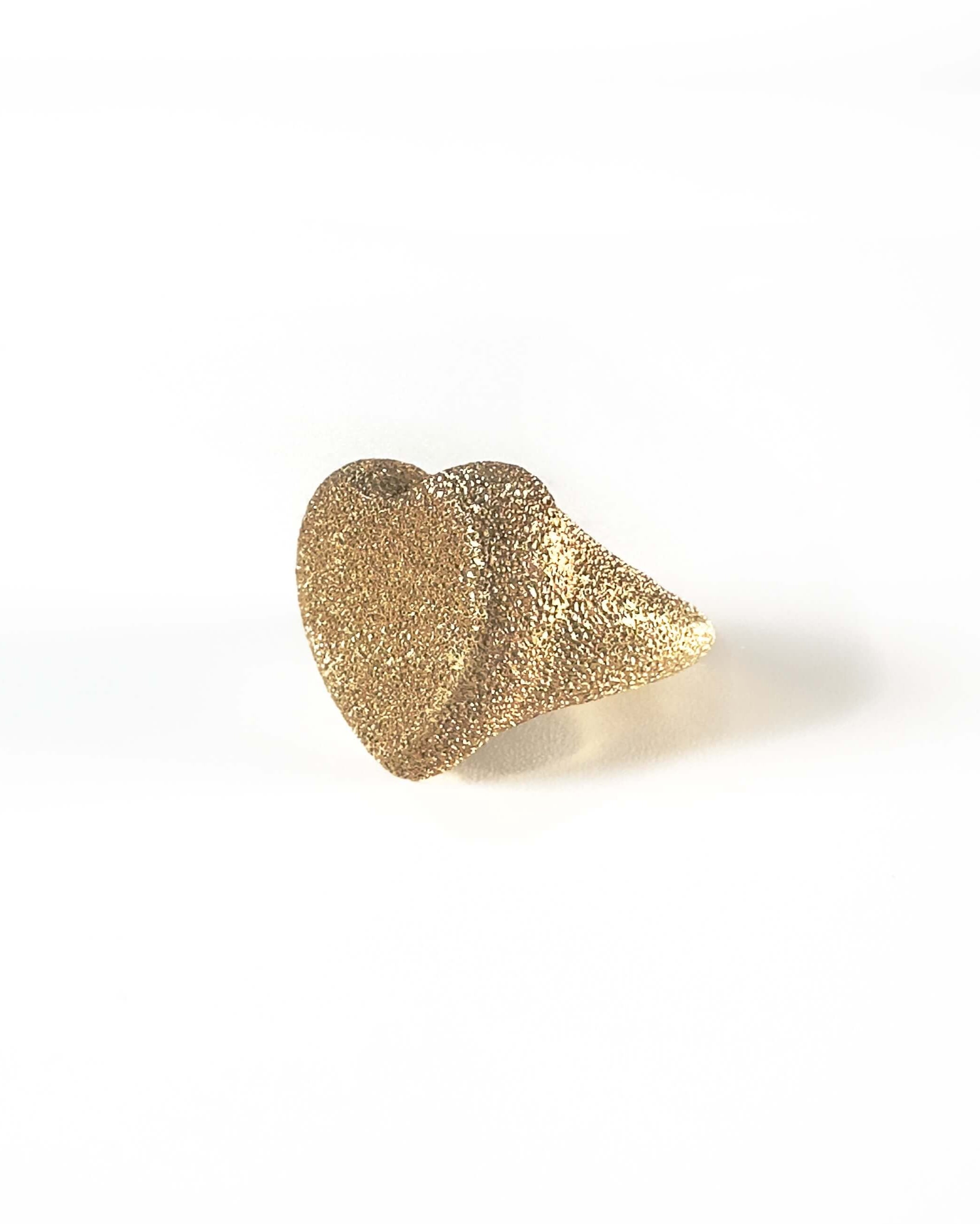Carolina Bucci gold ring in the shape of a heart , with a white background. The ring has a sparkle due to the texture. 