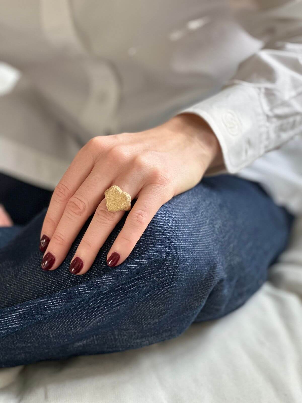 Model wearing Carolina Bucci gold heart ring hand on jeans