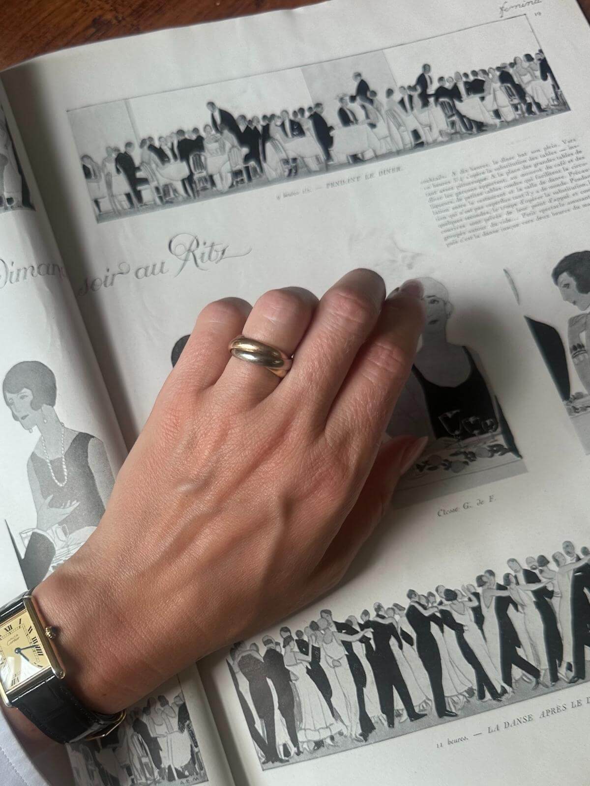 Hand with a Cartier Trinity ring on an open book with black and white illustrations