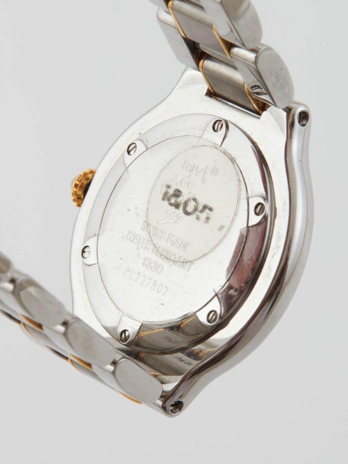 Close-up of a silver and gold Cartier watch with brand logo on back of face a light gray background