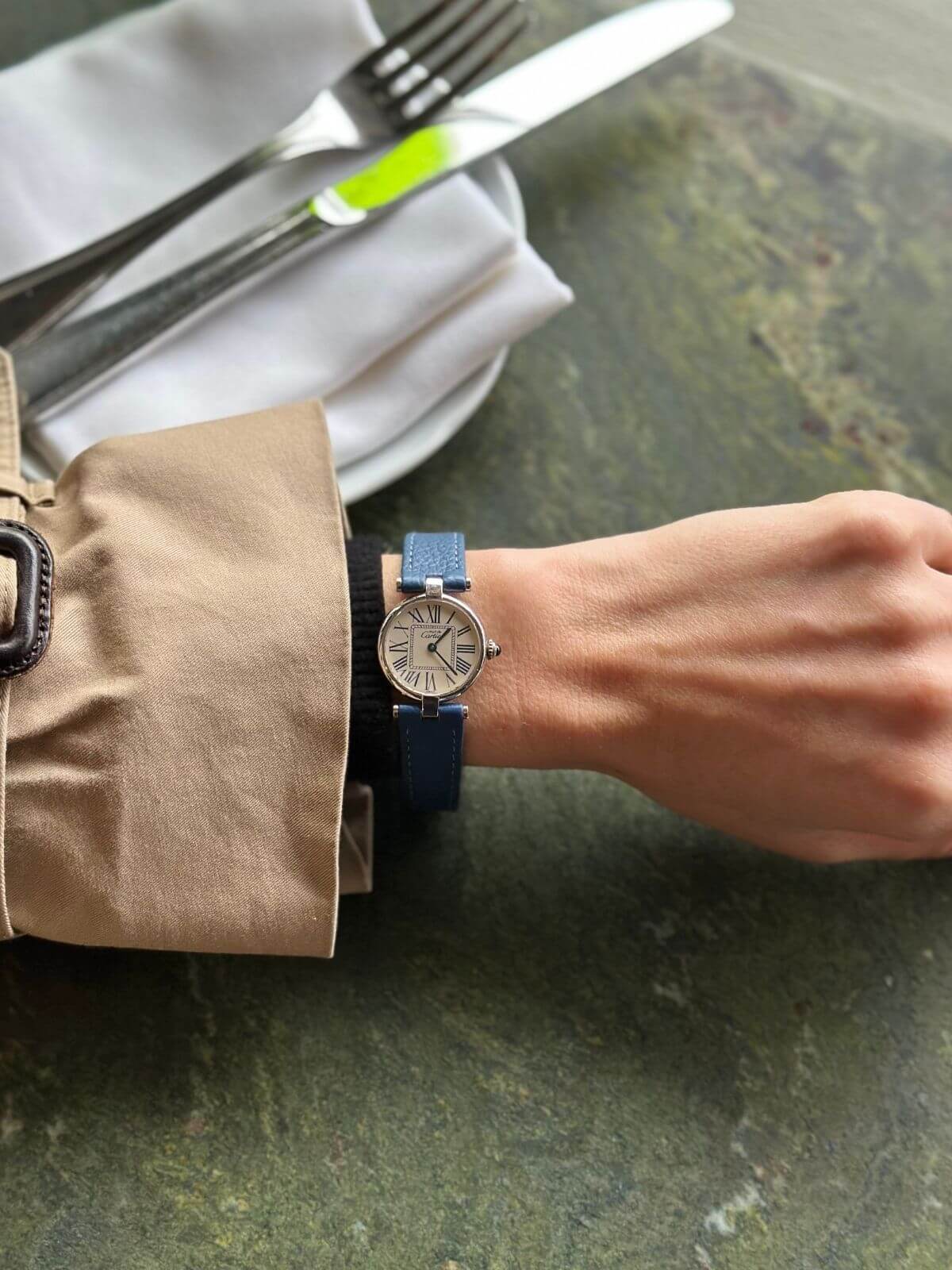 Person wearing a watch with a blue strap on a table setting with cutlery