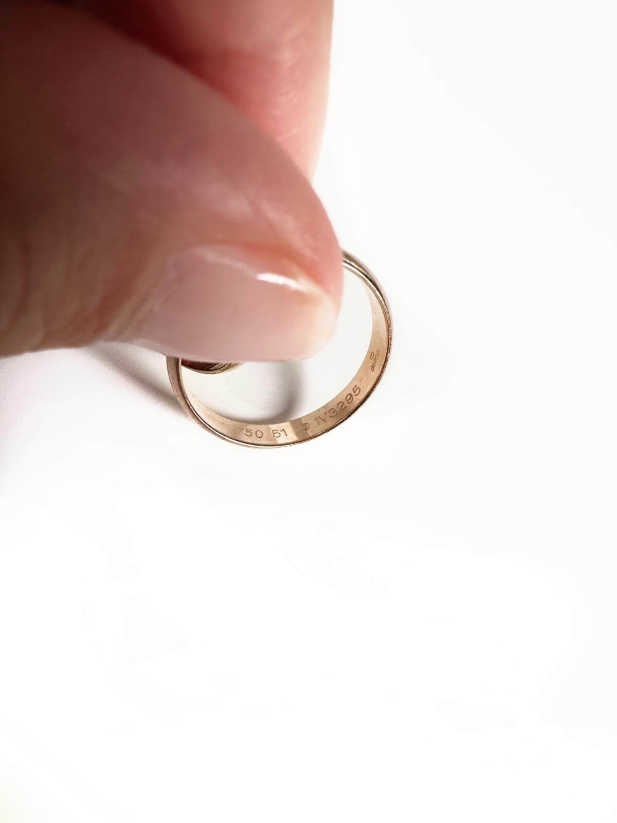 Cartier Trinity Gold ring being held showing serial number between a thumb and forefinger on a white background