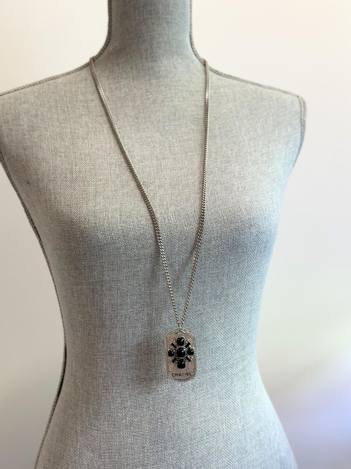 Louise Row Studio featuring Chanel long silver necklace with dog tag made with enamel design and CHANEL markings on body form.