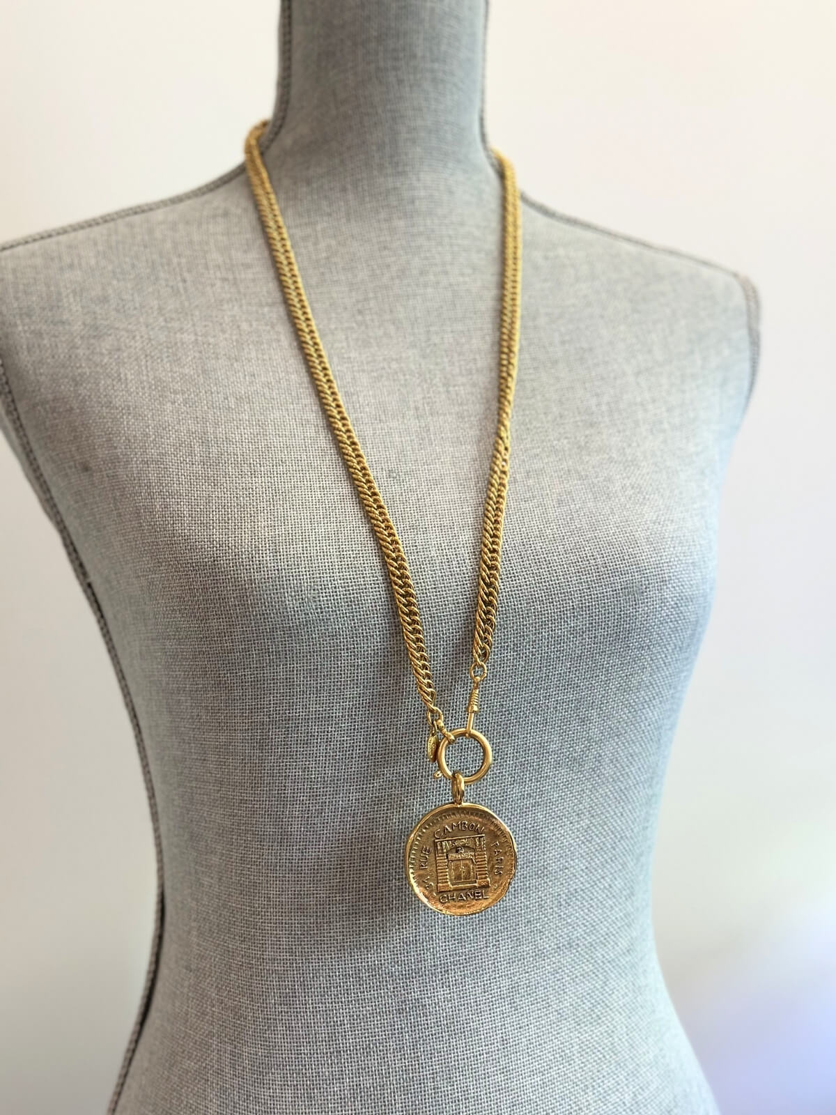Louise Row Studio featuring vintage Chanel rue de Cambon gold necklace with long chain and medallion on grey body form. 