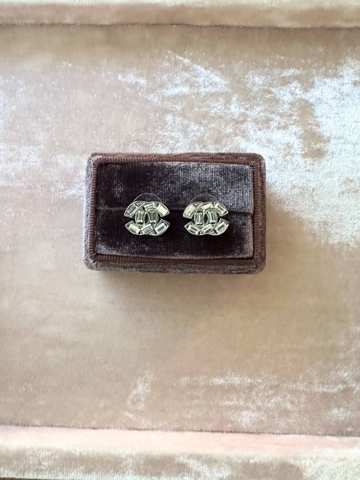 Louise Row Studio crystal Chanel earrings with a CC design on a brown display case and pink tray