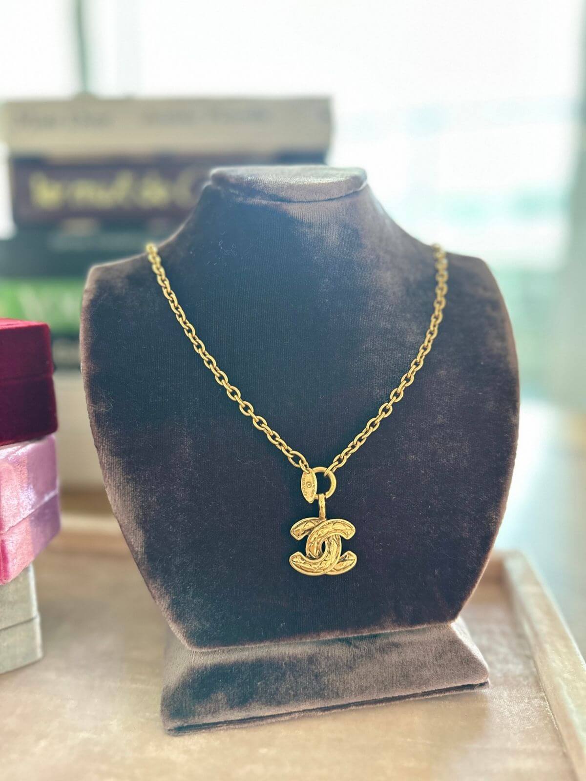 Chanel Gold necklace with a pendant on a dark gray velvet stand.