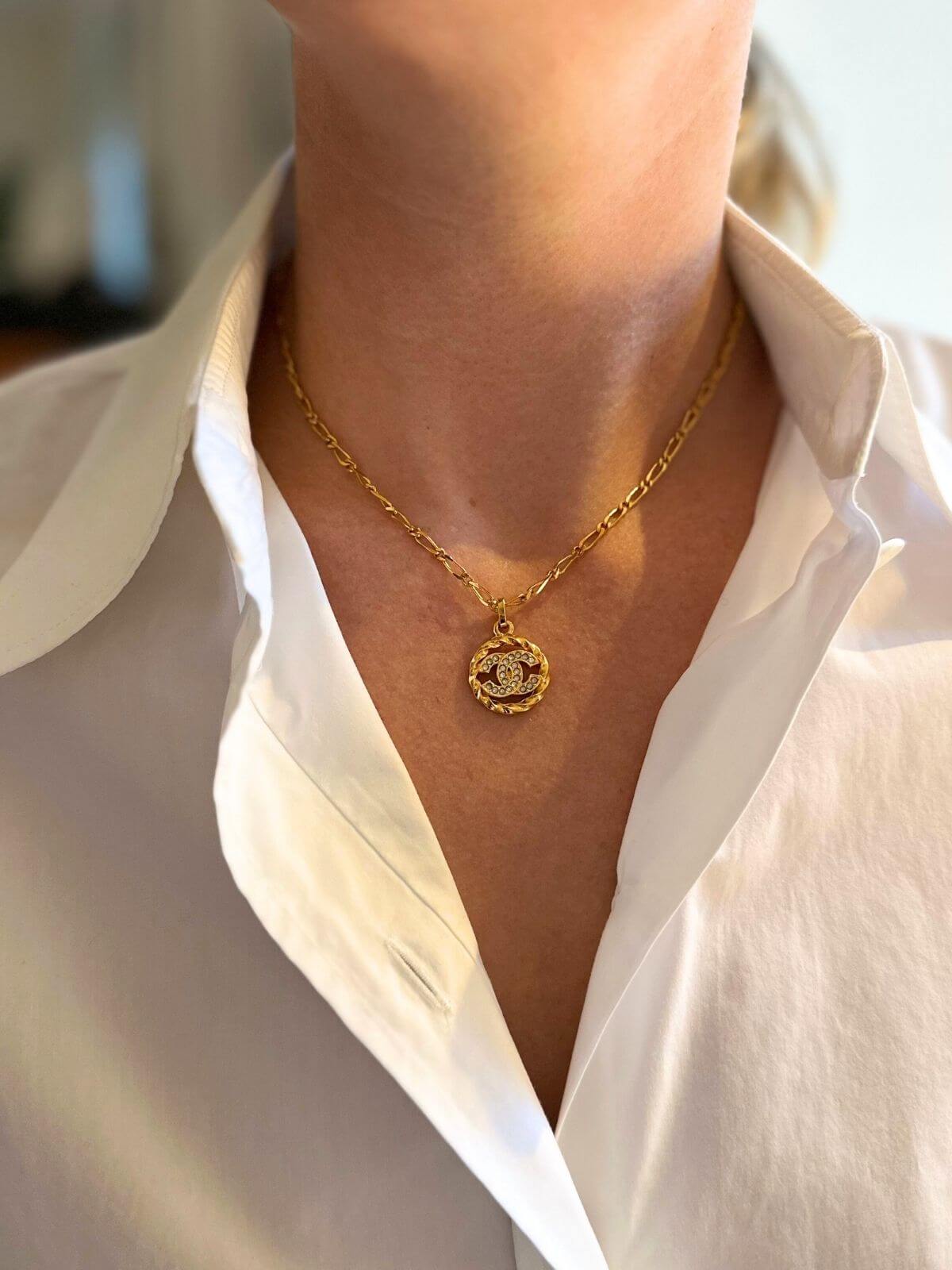 Gold necklace with a pendant worn by a person in a white shirt.