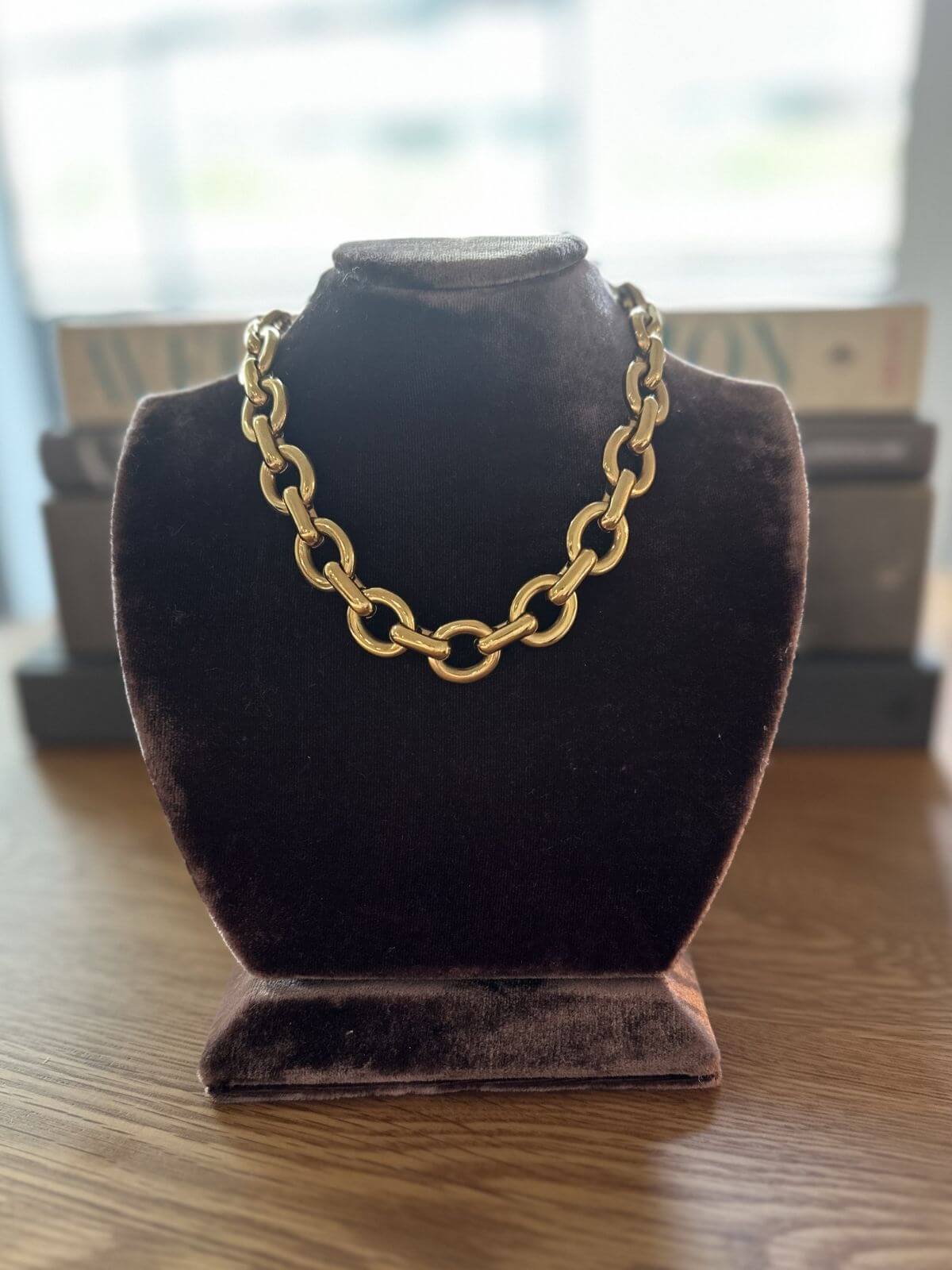 Gold chain necklace on a purple velvet bust against a blurred indoor background