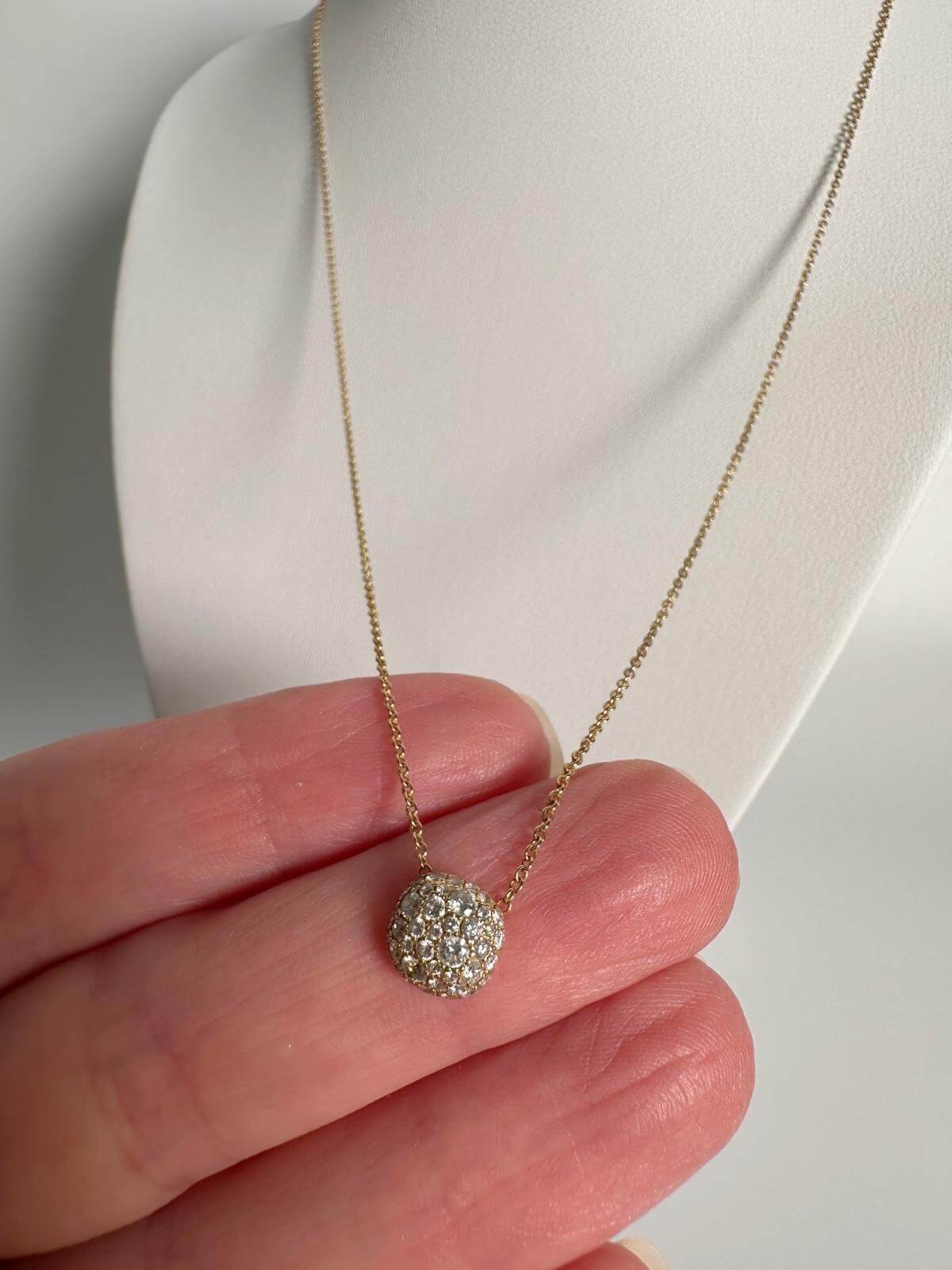DY Gold necklace with a diamond pendant held by a hand against a white background