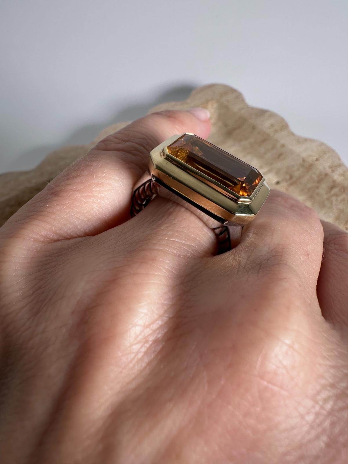 DY citrine and Gold ring with a large brown gemstone on a hand against a neutral background