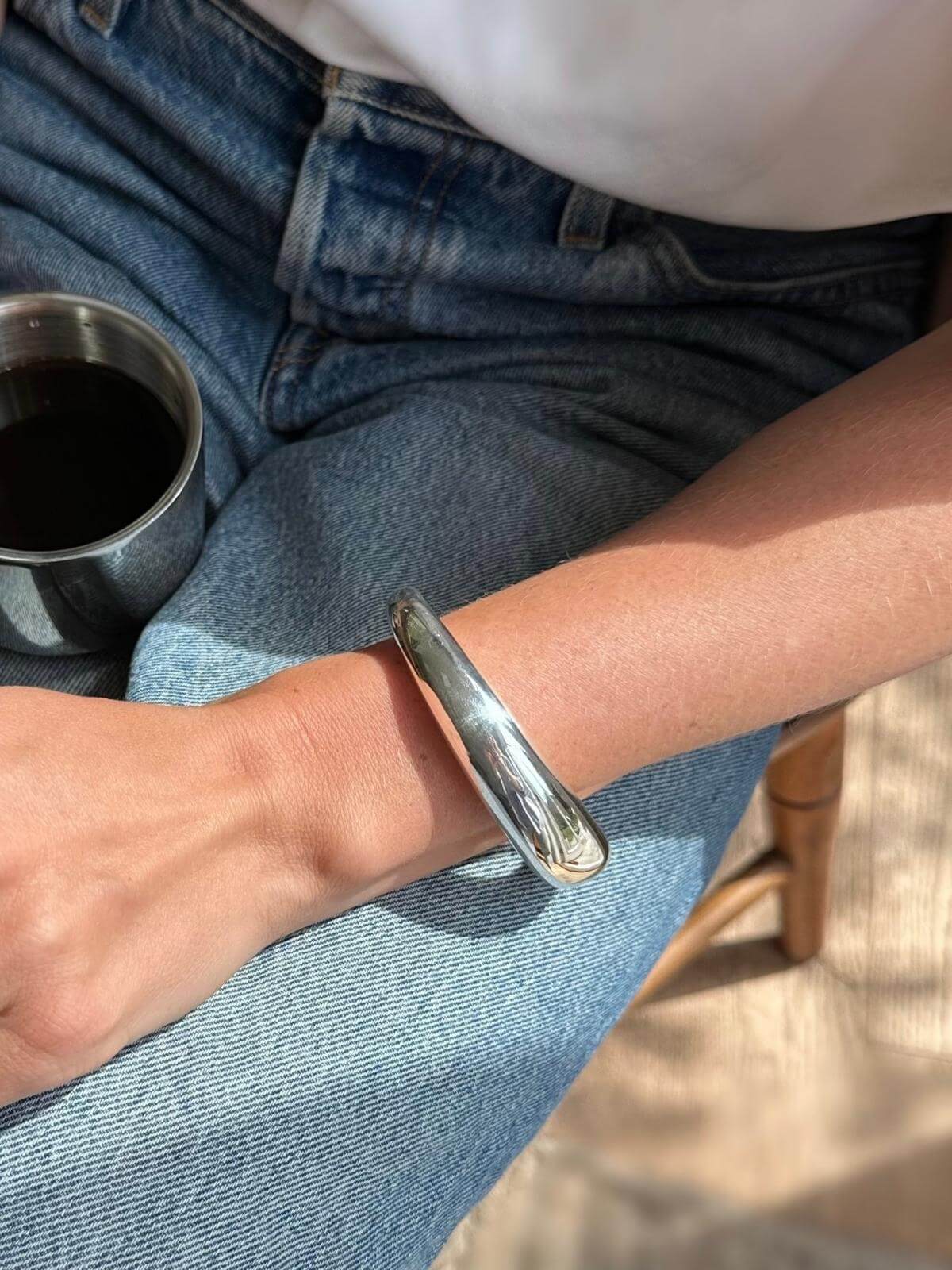 Model wearing DY silver bangle with jeans on wooden chair