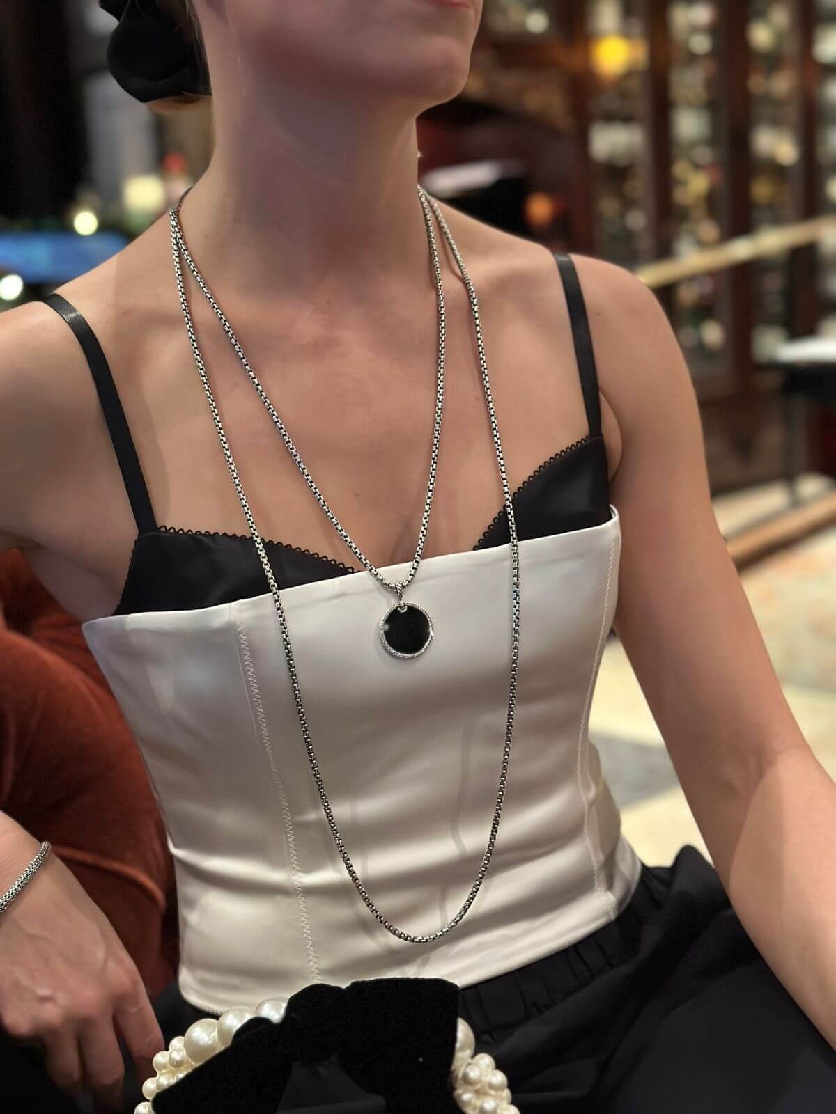 Person wearing a white top with black straps and a long necklace.