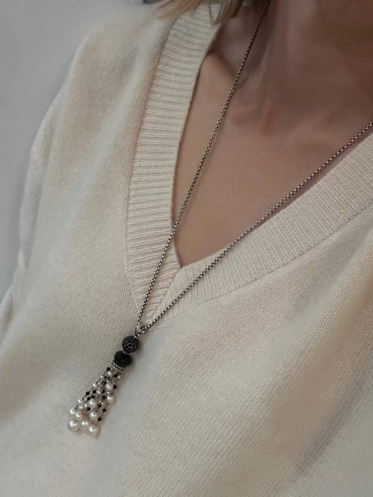 DY pendant shown on silver chain with black and silver beads on a person wearing a beige sweater.