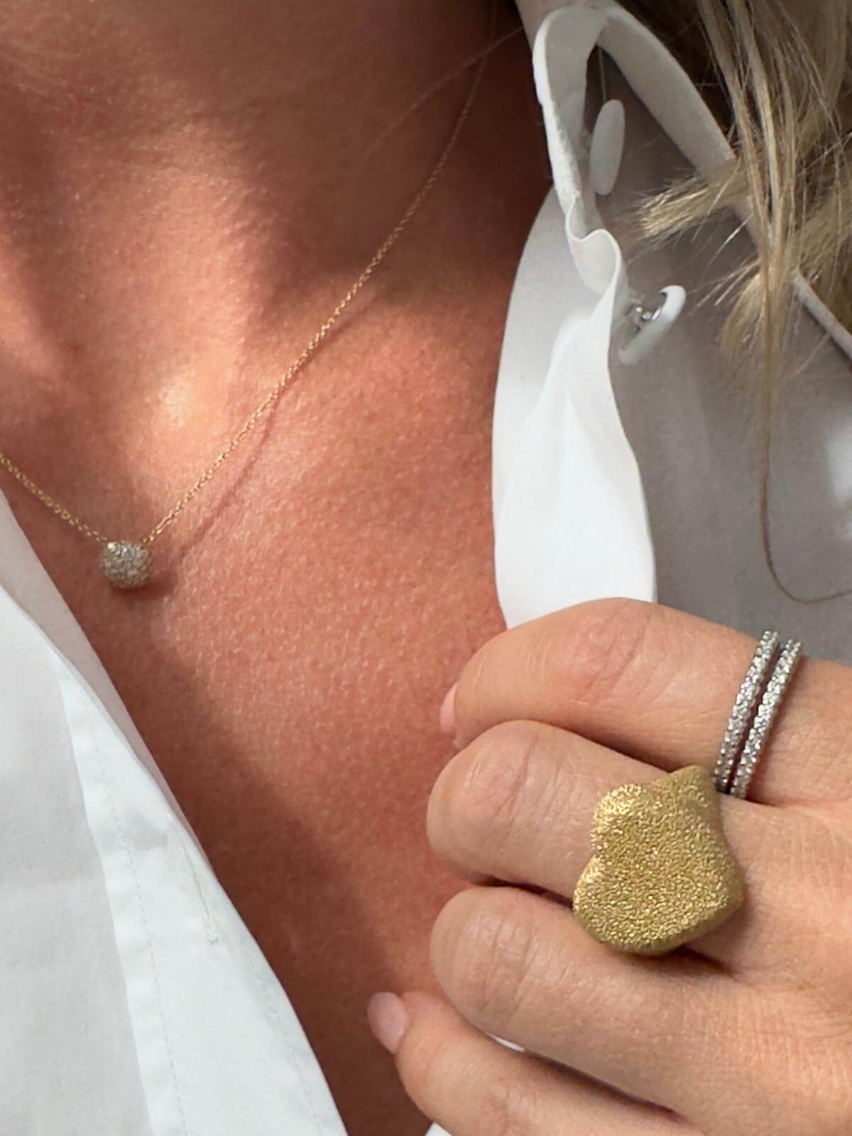 Close-up of a person wearing a DY gold  necklace, with a blurred background.