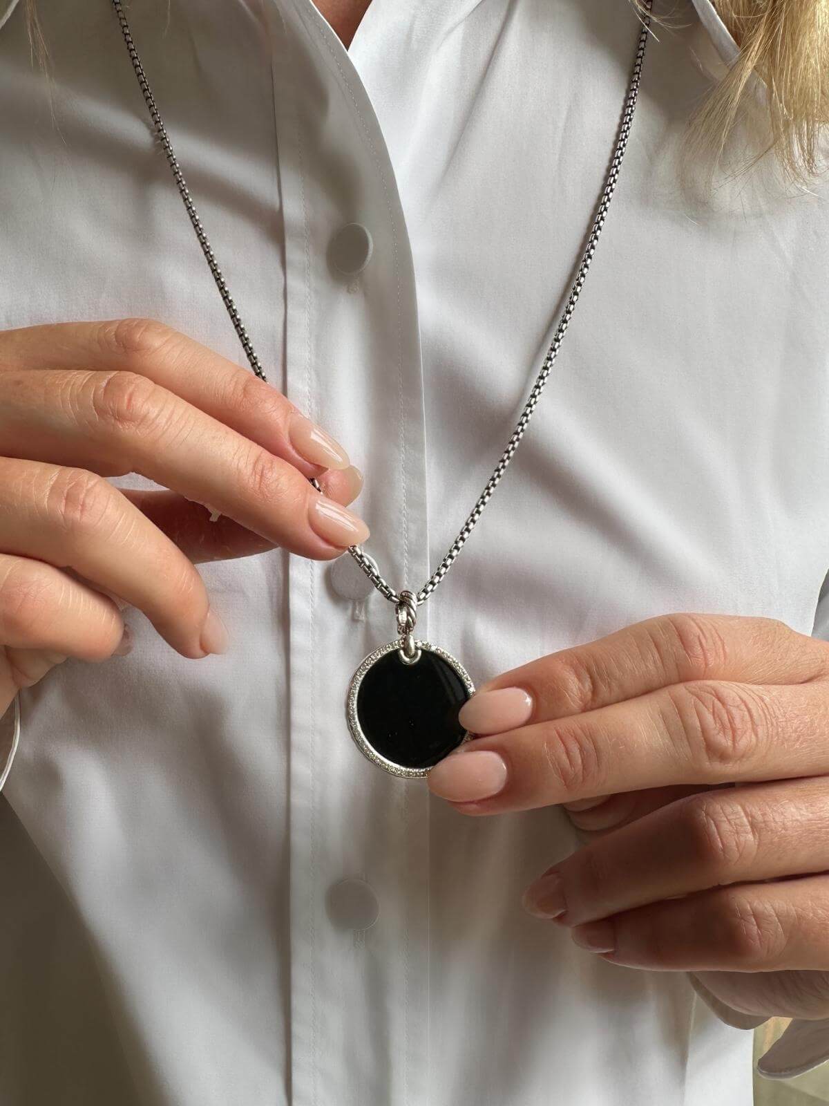 DY black onyx pendant and chain with  on a white shirt with a model hands holding the pendant out from the shirt to highlight 